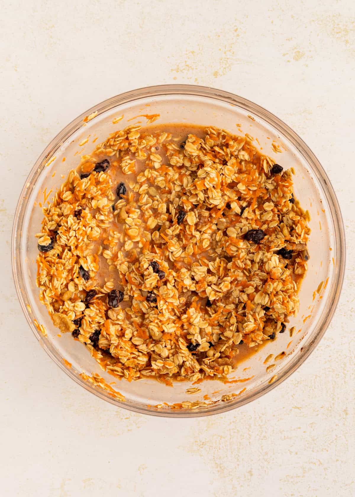 A glass bowl filled with oatmeal, raisins, and a wet mixture, ready to be baked.