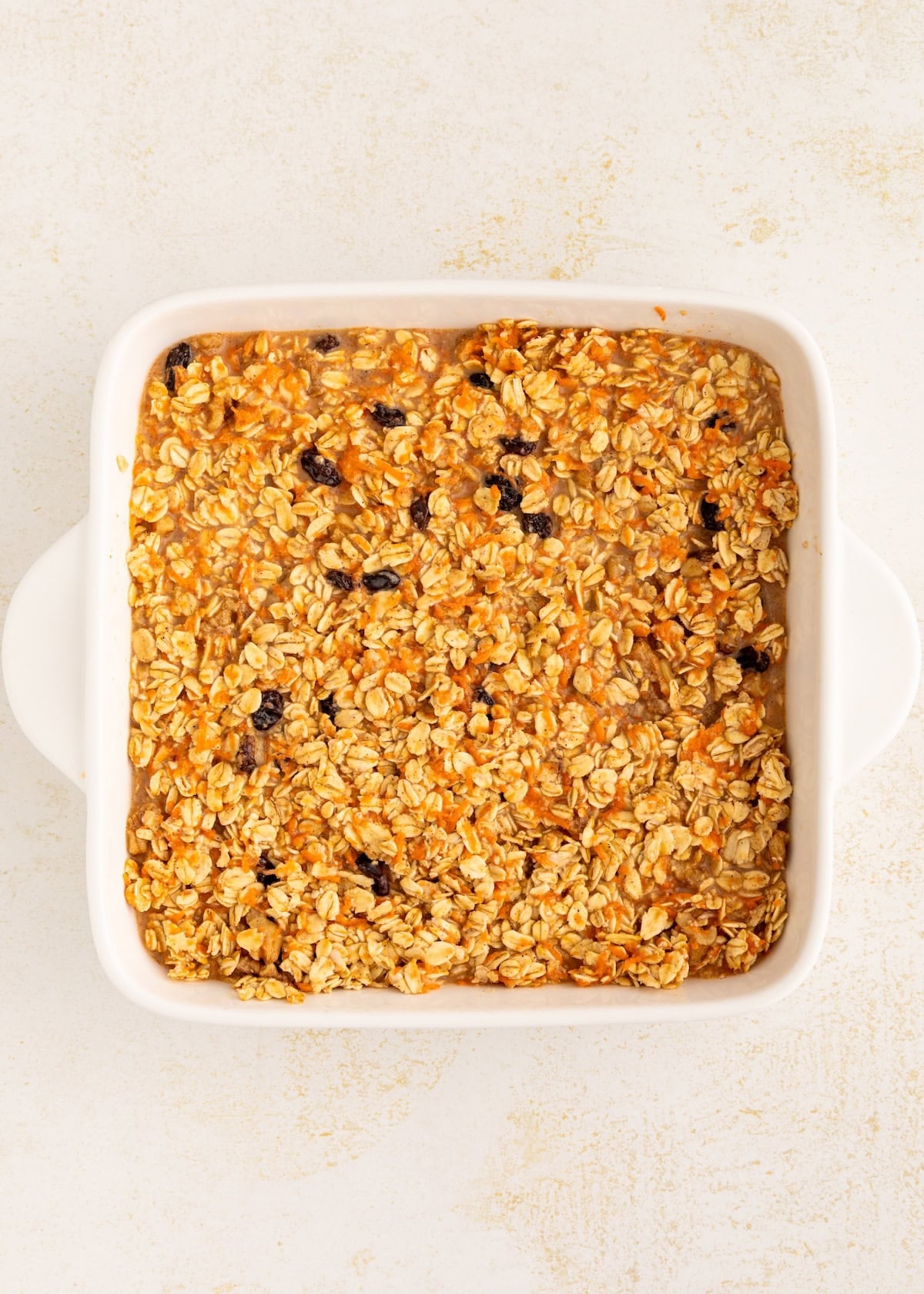 Baked oatmeal with raisins in a white square baking dish on a light background.