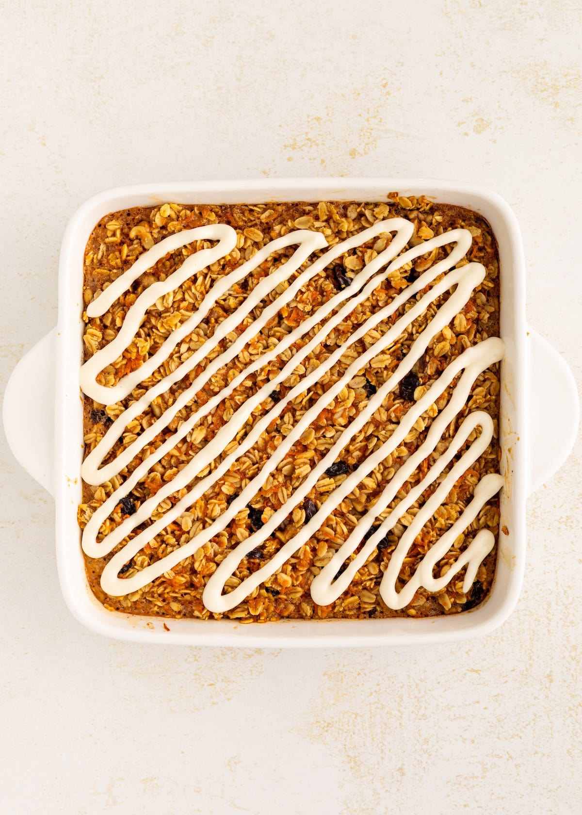 Baked oatmeal topped with a zigzag drizzle of white icing in a square white dish.