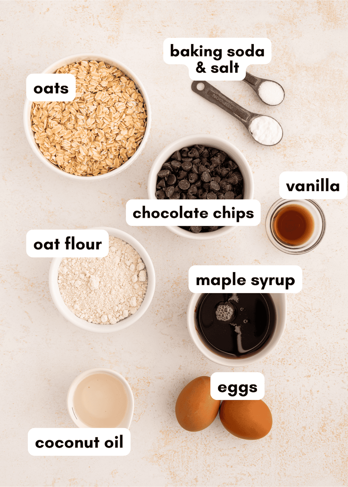 Bowls of oats, oat flour, chocolate chips, eggs, maple syrup, coconut oil, vanilla, and spices.