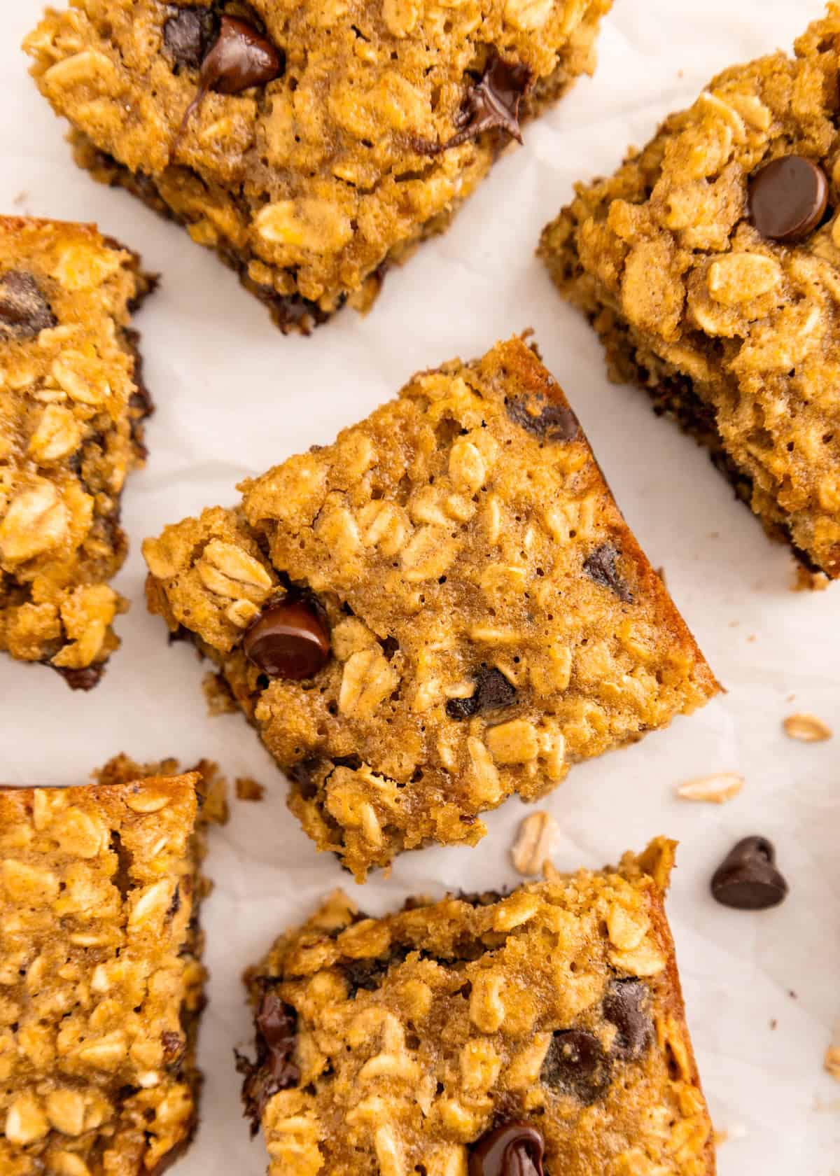 Five oatmeal chocolate chip bars on parchment paper, viewed from above.