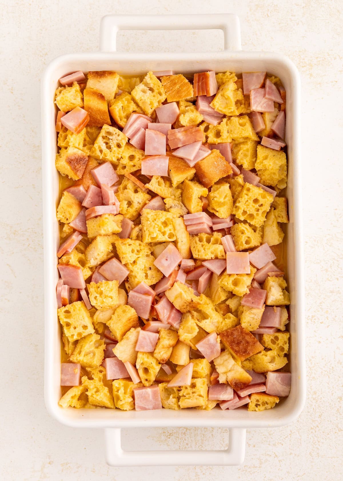 Casserole dish with cubed bread and diced ham pieces arranged evenly.