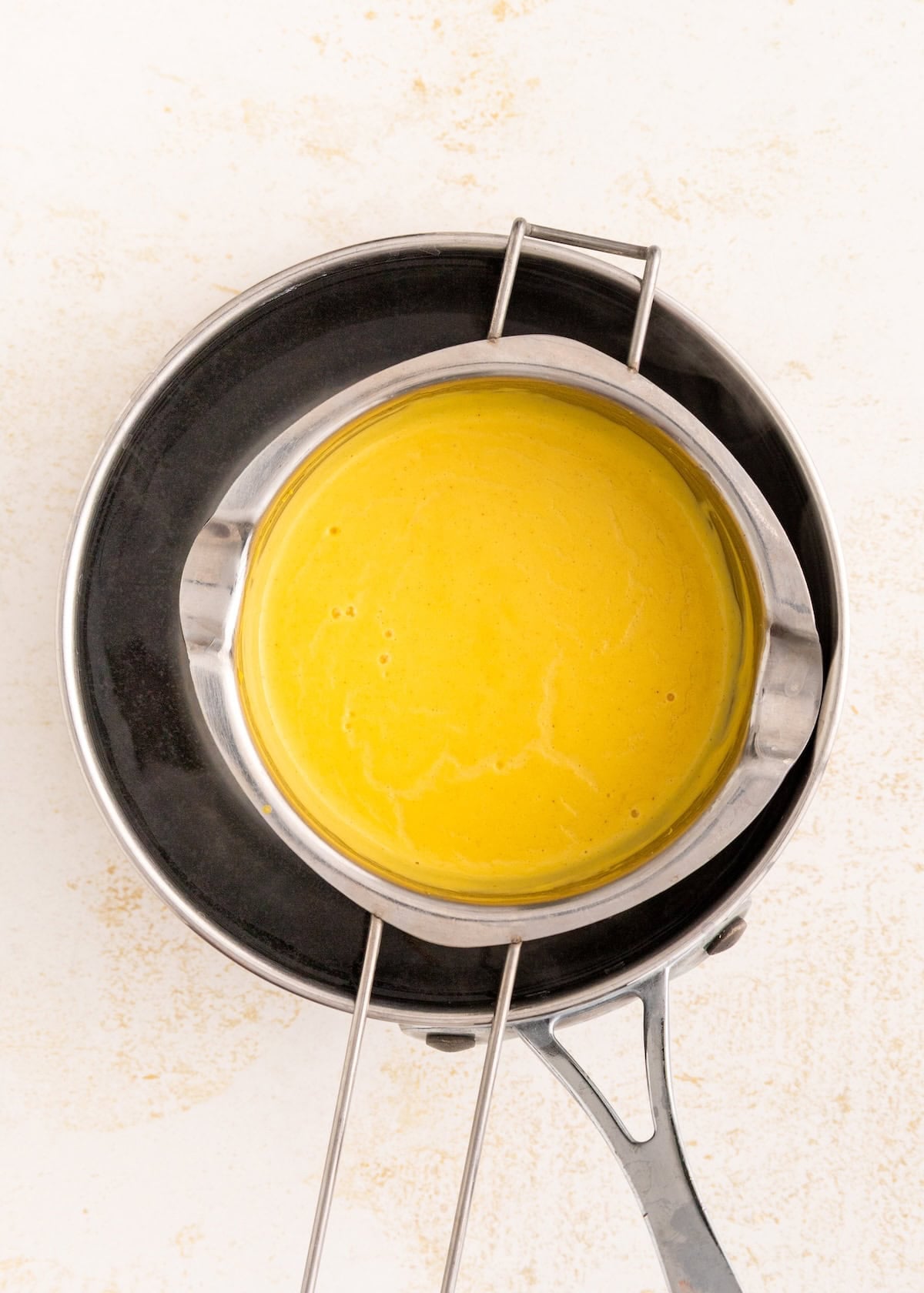 A metal bowl with yellow sauce sits over a pot of hot water, forming a double boiler.