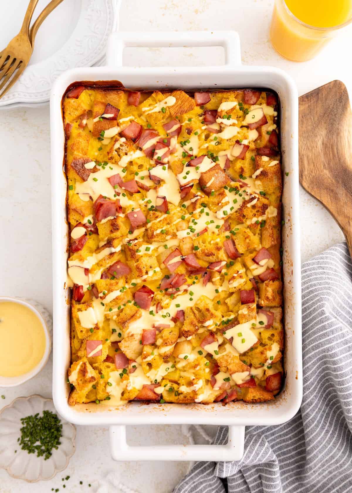 Baked breakfast casserole with bread, ham, cheese, and chives in a white dish.