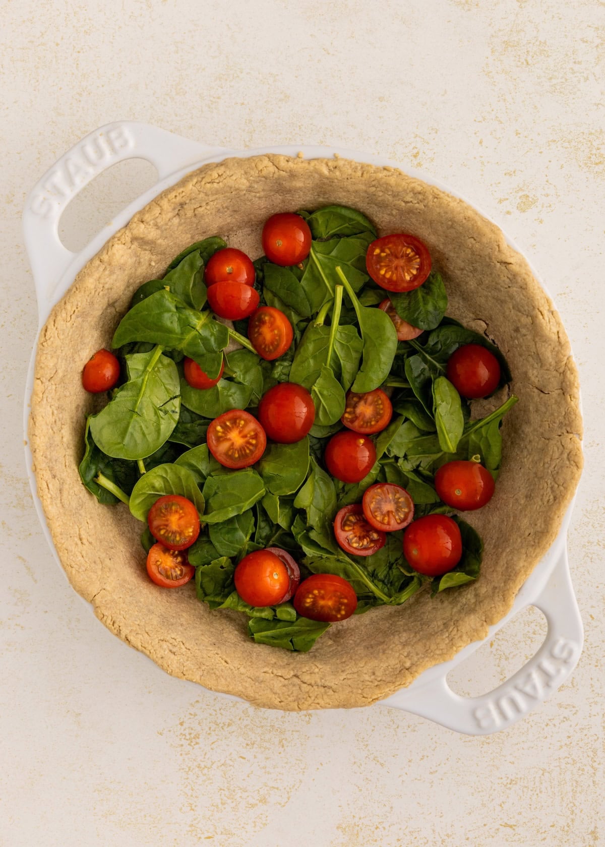 Unbaked pie crust filled with fresh spinach leaves and halved cherry tomatoes.