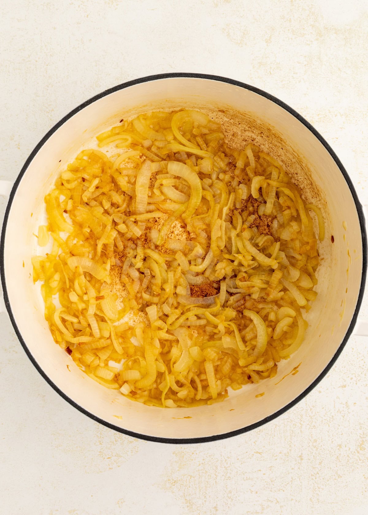 Sliced onions cooking in a white pot, lightly browned and softened.