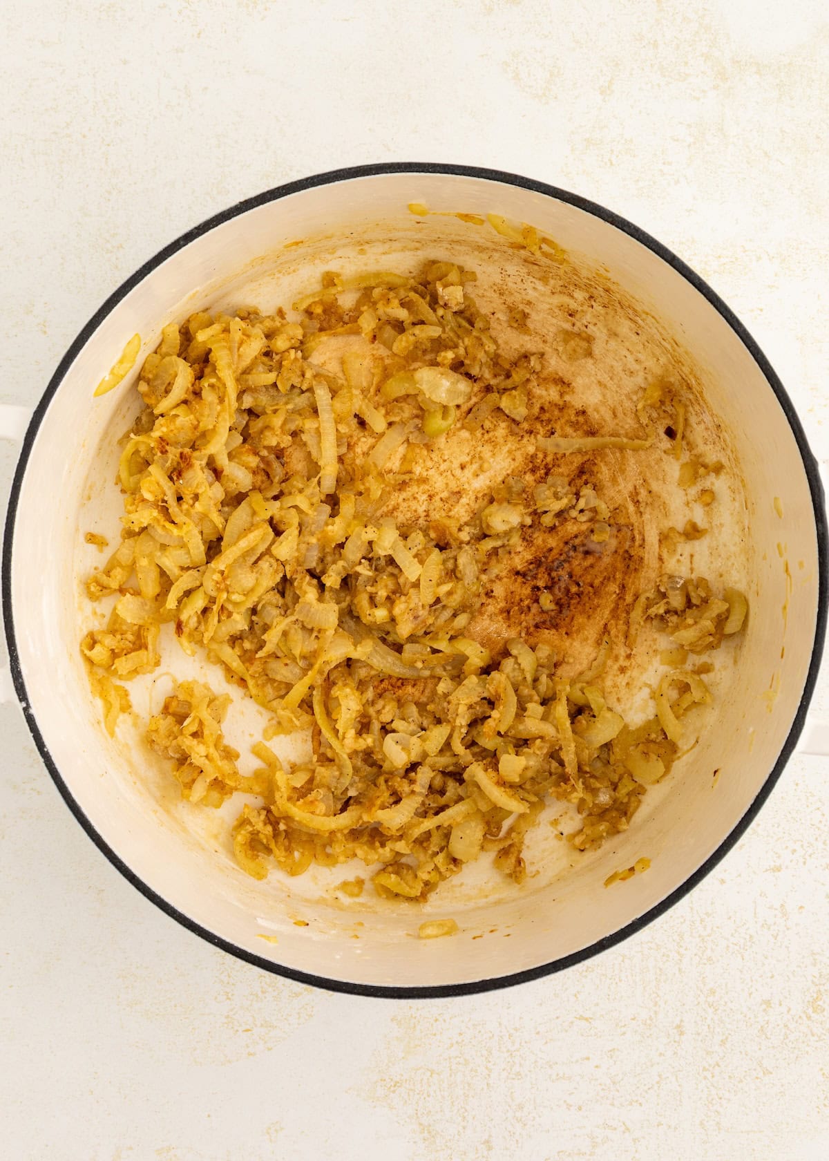 Sautéed onions in a white pot with browned bits stuck to the bottom.