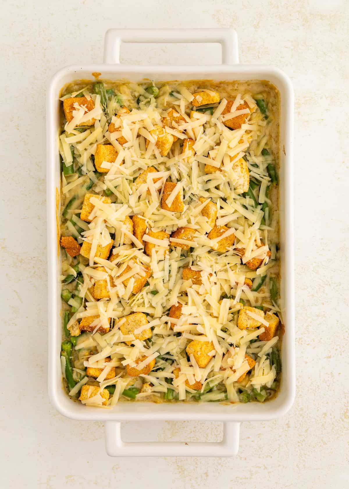 Casserole dish with spinach, croutons, and shredded cheese ready for baking.