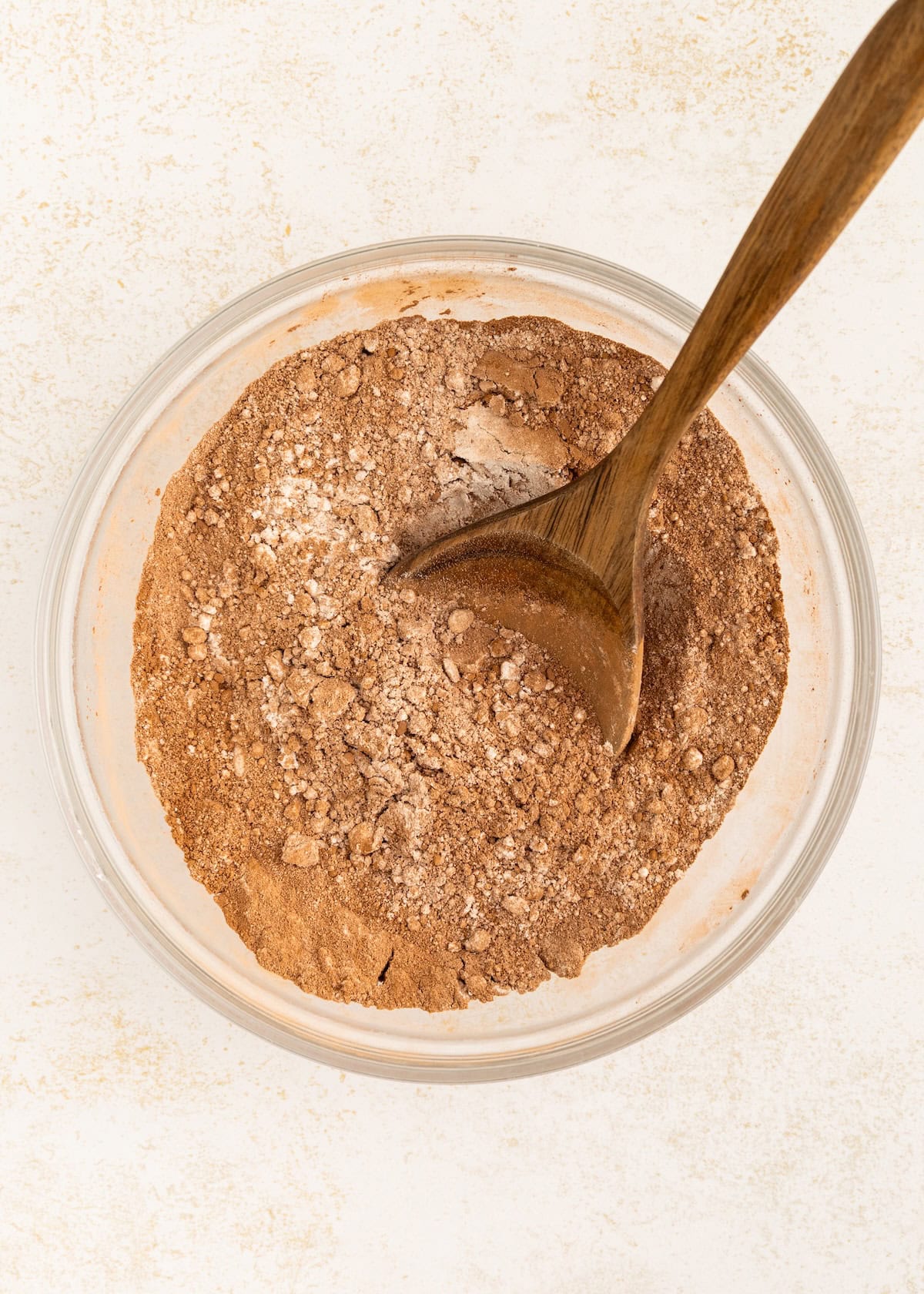 Glass bowl with cocoa powder and flour mixture, stirred with a wooden spoon.
