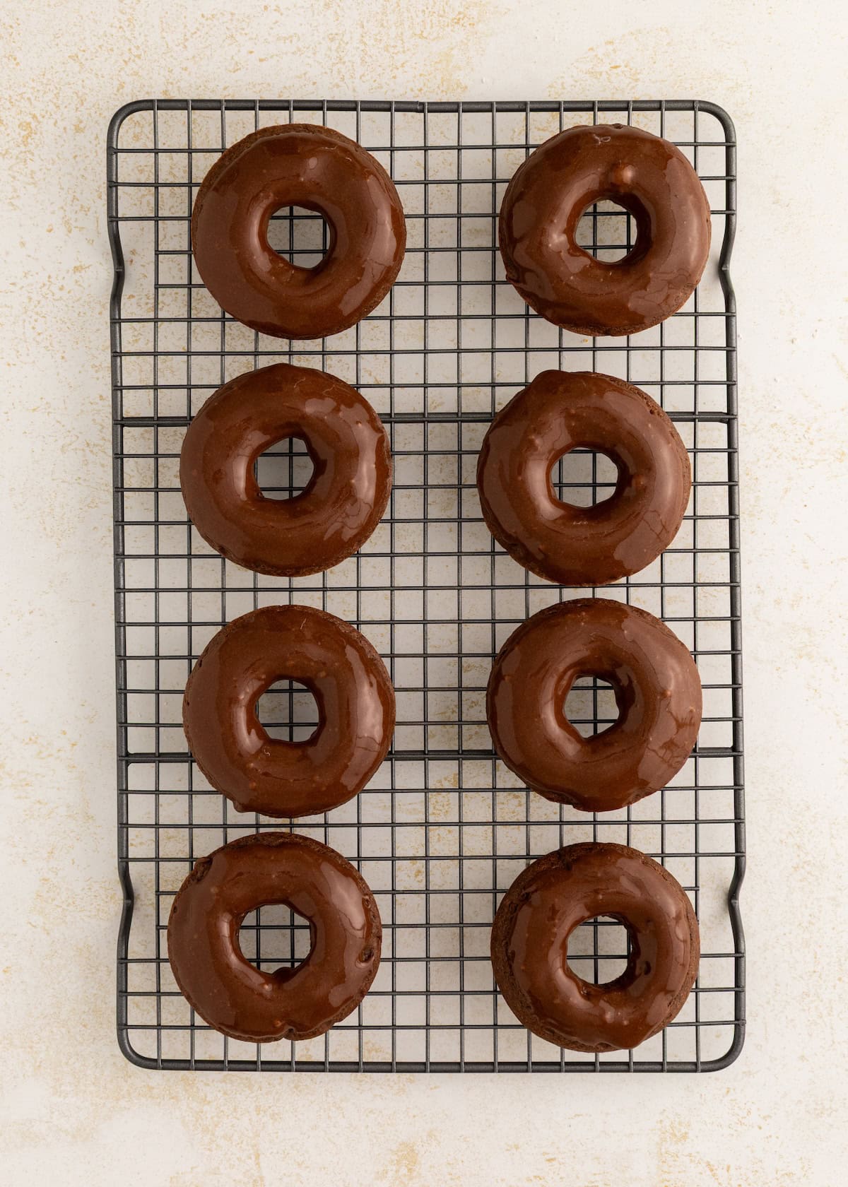 Eight chocolate-glazed donuts on a cooling rack, arranged in two neat columns.