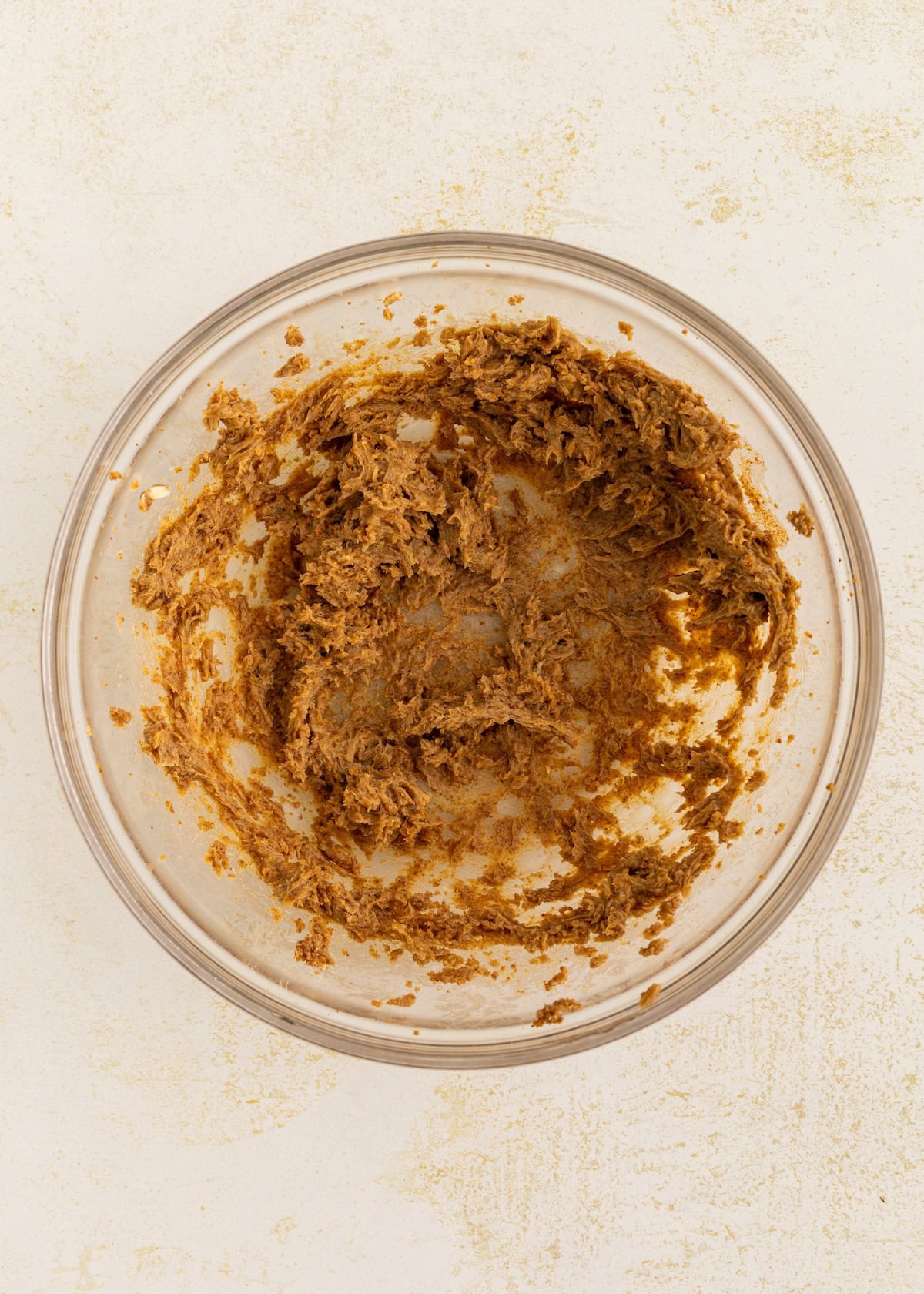 Brown sugar and butter mixture in a glass bowl on a light surface.