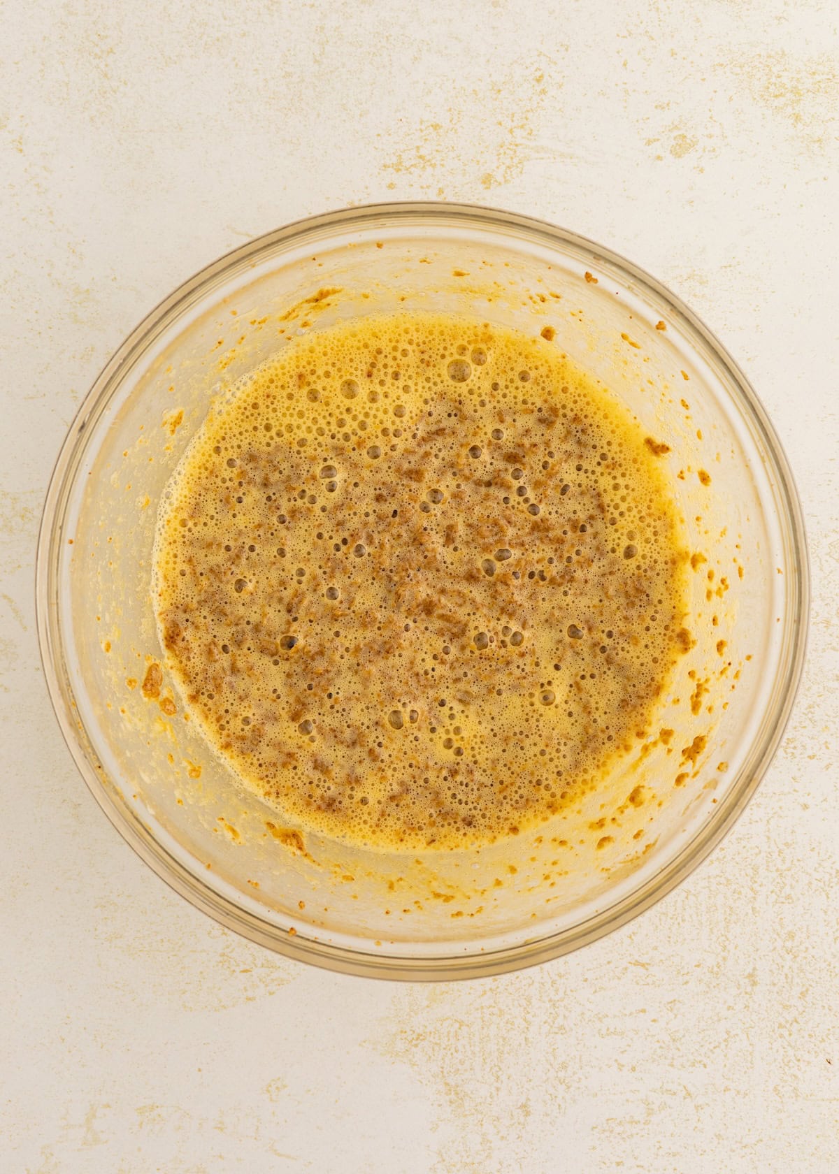 A glass bowl with a frothy, brownish-orange liquid mixture on a light surface.