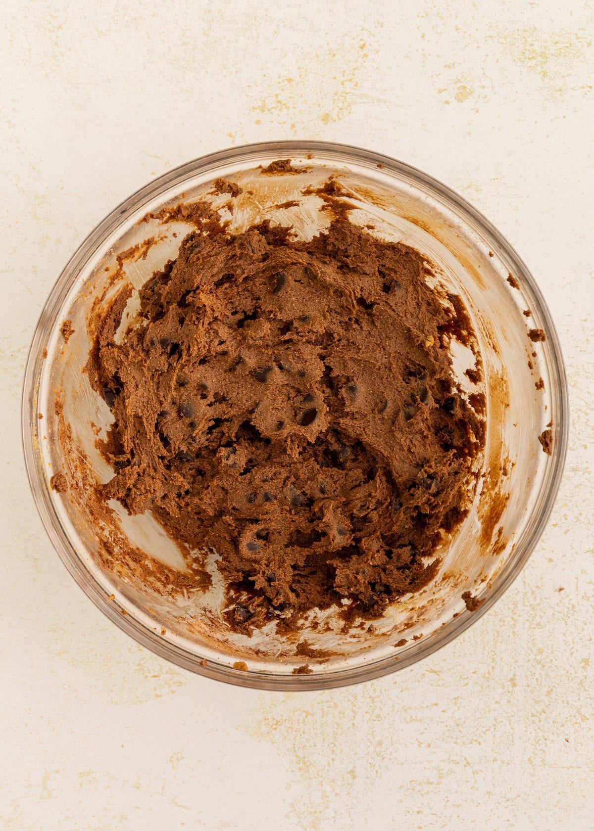 Chocolate cookie dough with chocolate chips in a glass bowl on a light surface.
