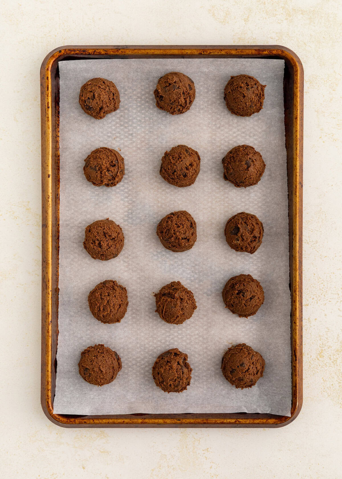 A baking sheet with 16 evenly spaced scoops of chocolate cookie dough on parchment paper.