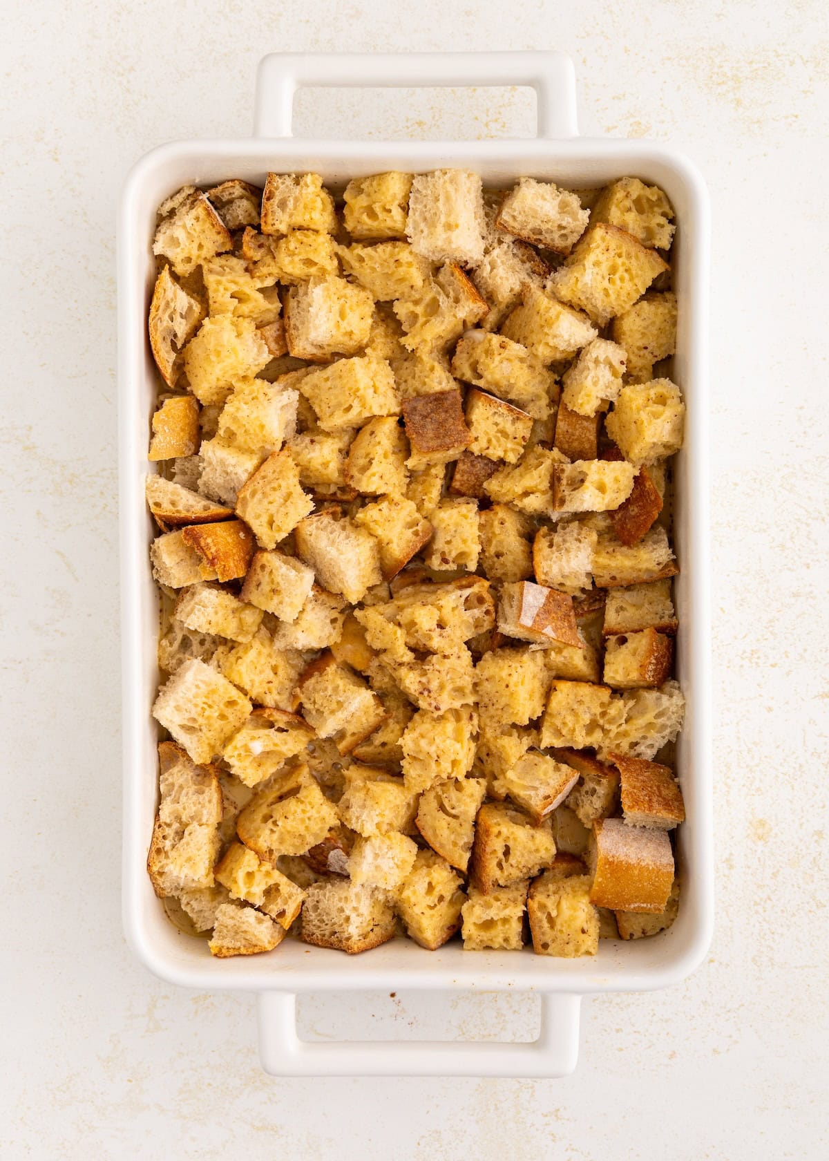 Cubed bread pieces in a white rectangular baking dish on a light background.