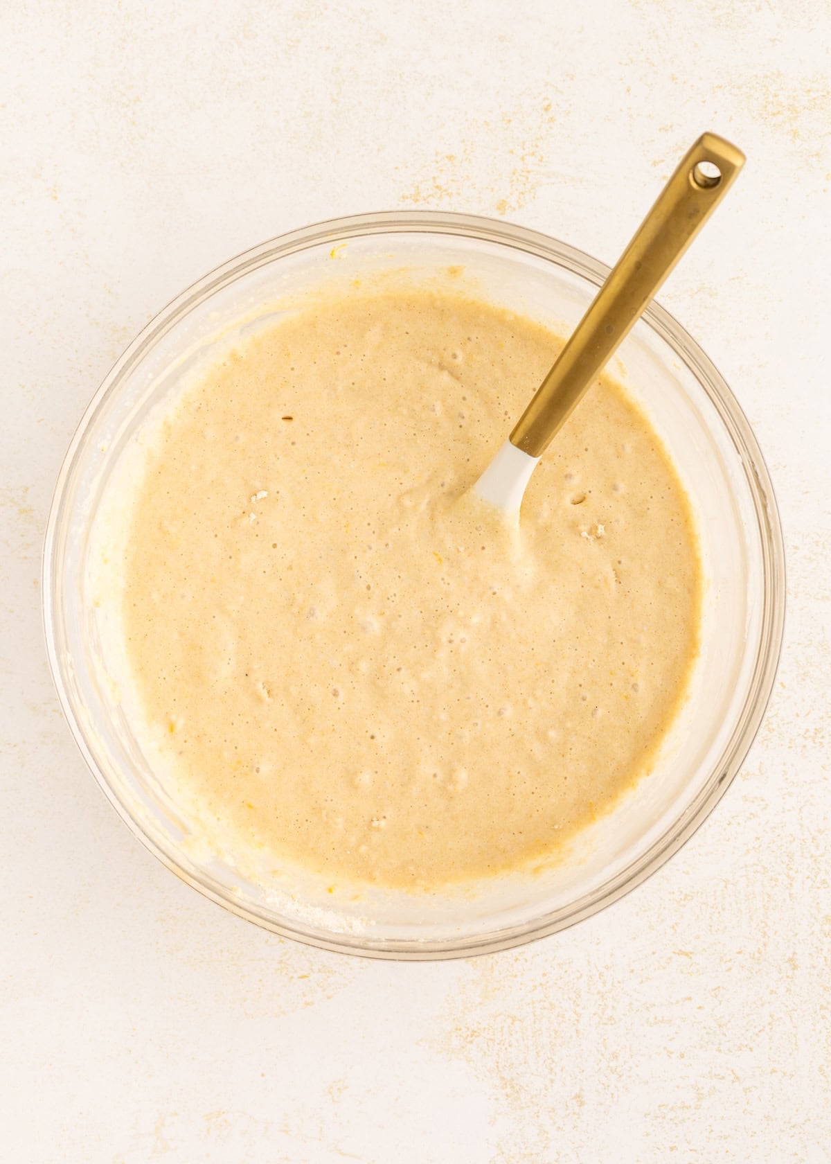 Bowl of pancake batter with a spatula on a light surface.