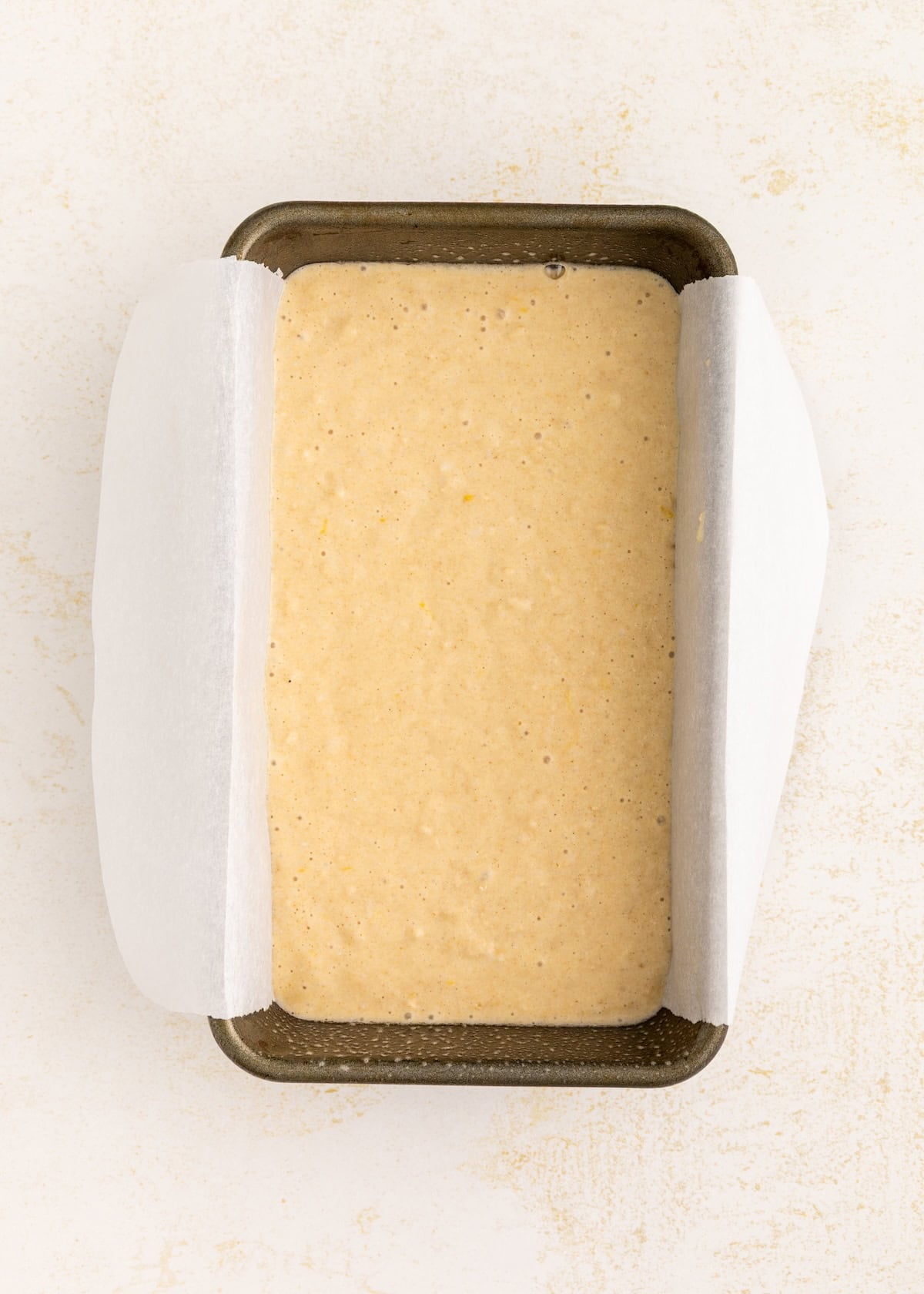Banana bread batter in a loaf pan lined with parchment paper, ready to be baked.