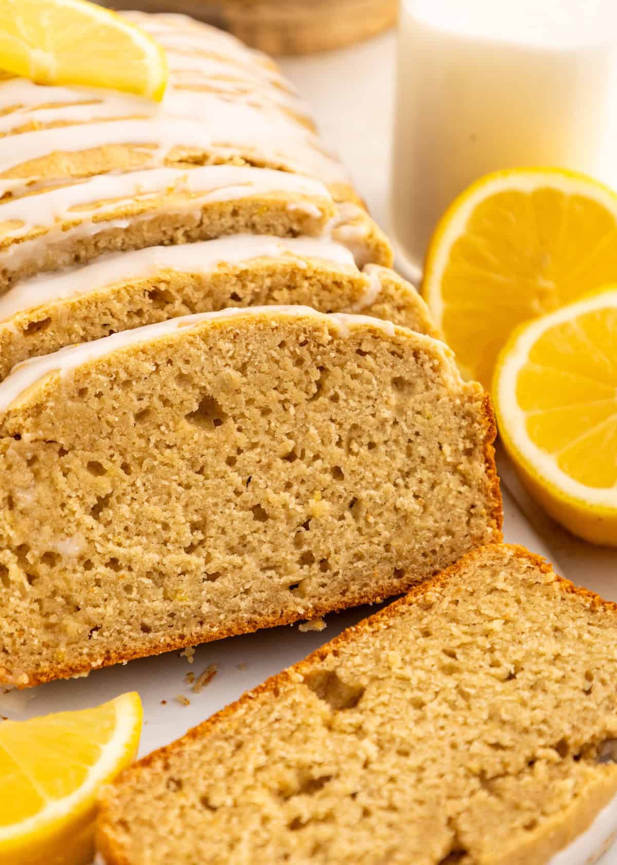 Sliced lemon bread with icing, garnished with lemon slices, next to a glass of milk.