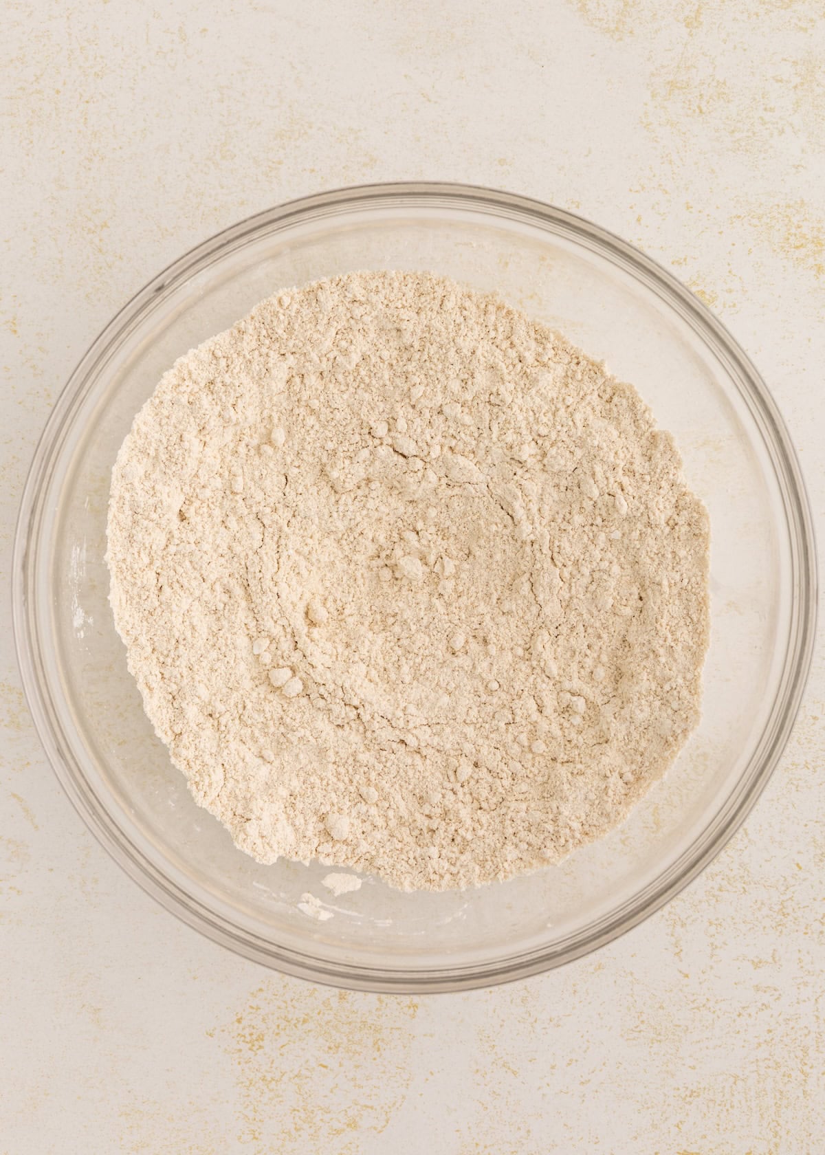 A glass bowl filled with a mixture of dry flour on a light-colored surface.