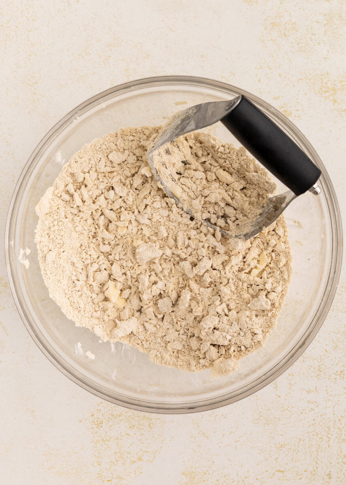 Glass bowl with flour mixture and a pastry cutter blending butter into the dry ingredients.