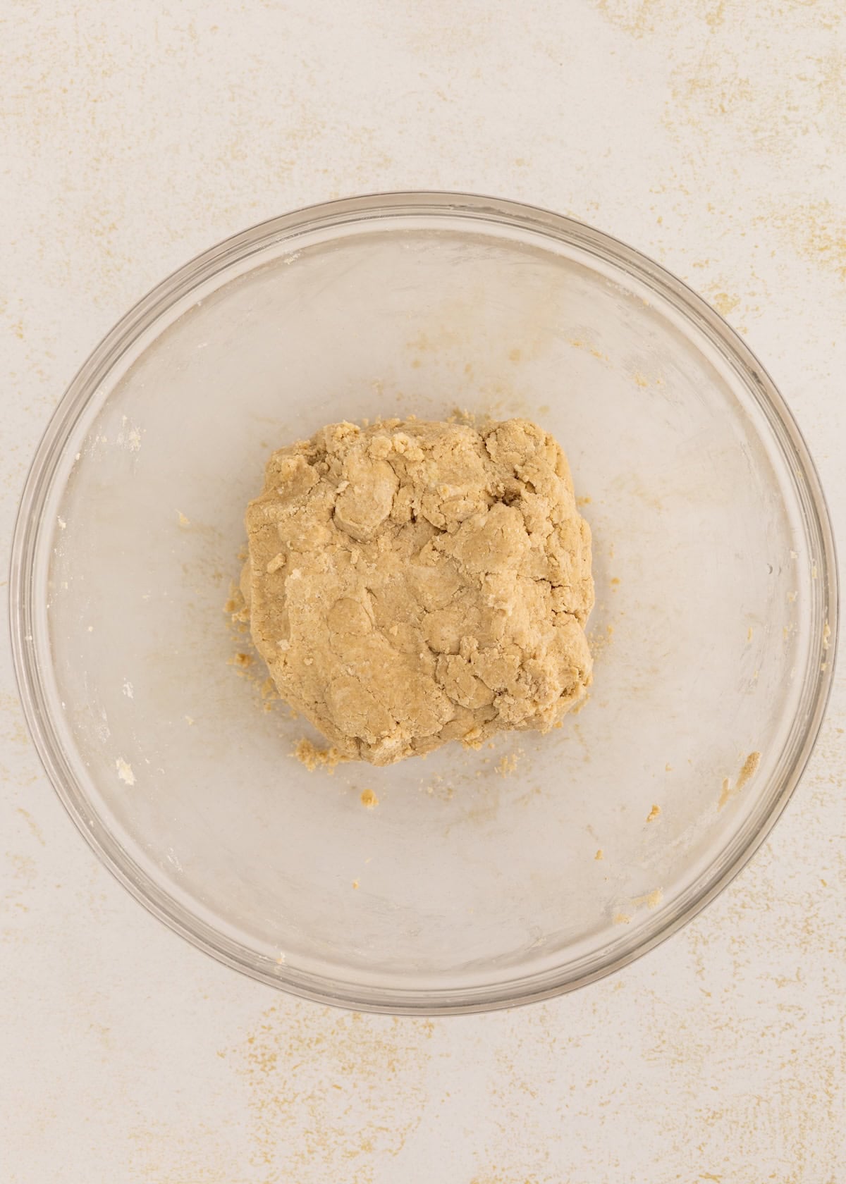 A ball of cookie dough in a clear glass bowl on a light-colored surface.
