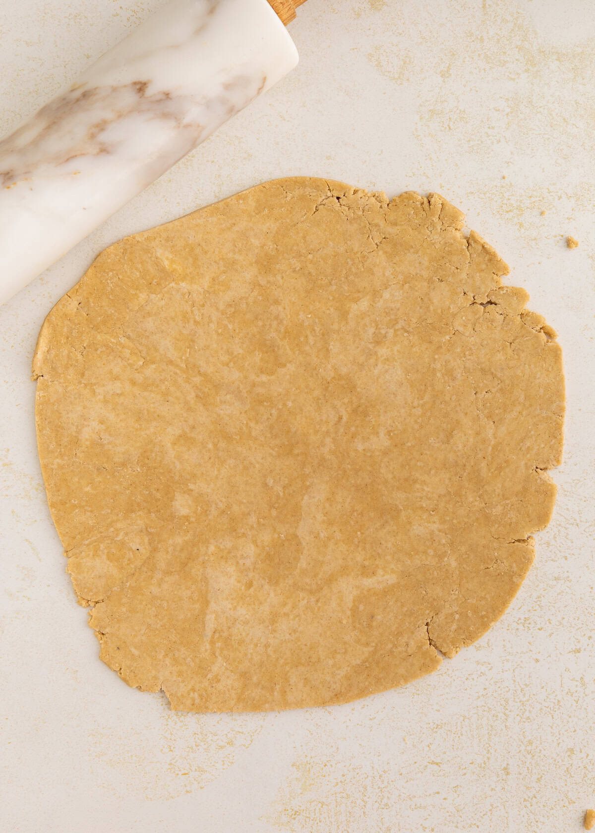 Round sheet of dough rolled out on a lightly floured surface with a marble rolling pin.