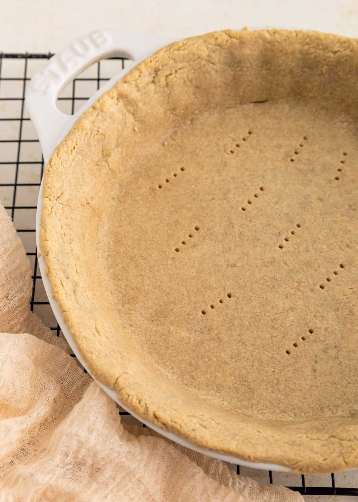 Unbaked pie crust in a white pie dish, with fork marks, on a cooling rack.