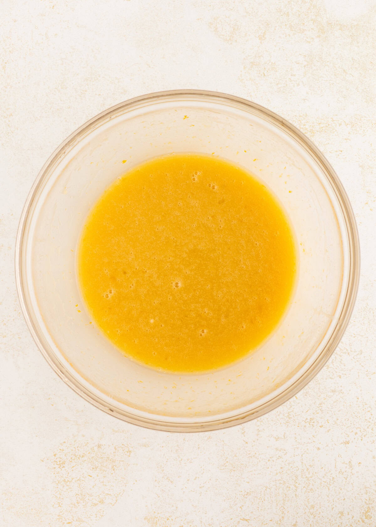 A glass bowl filled with yellow liquid batter on a light surface.