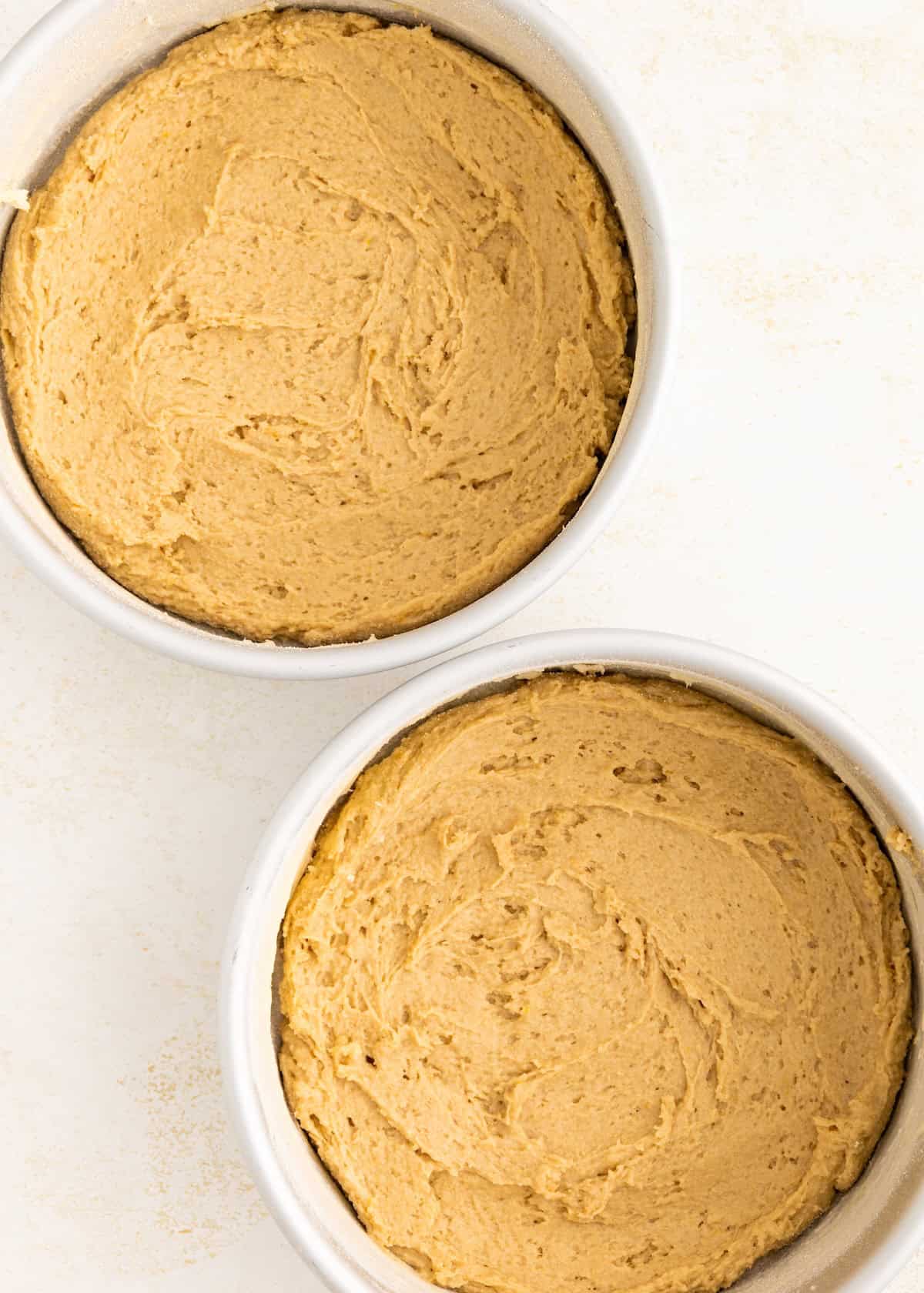 Two round cake pans filled with unbaked brown cake batter on a light surface.