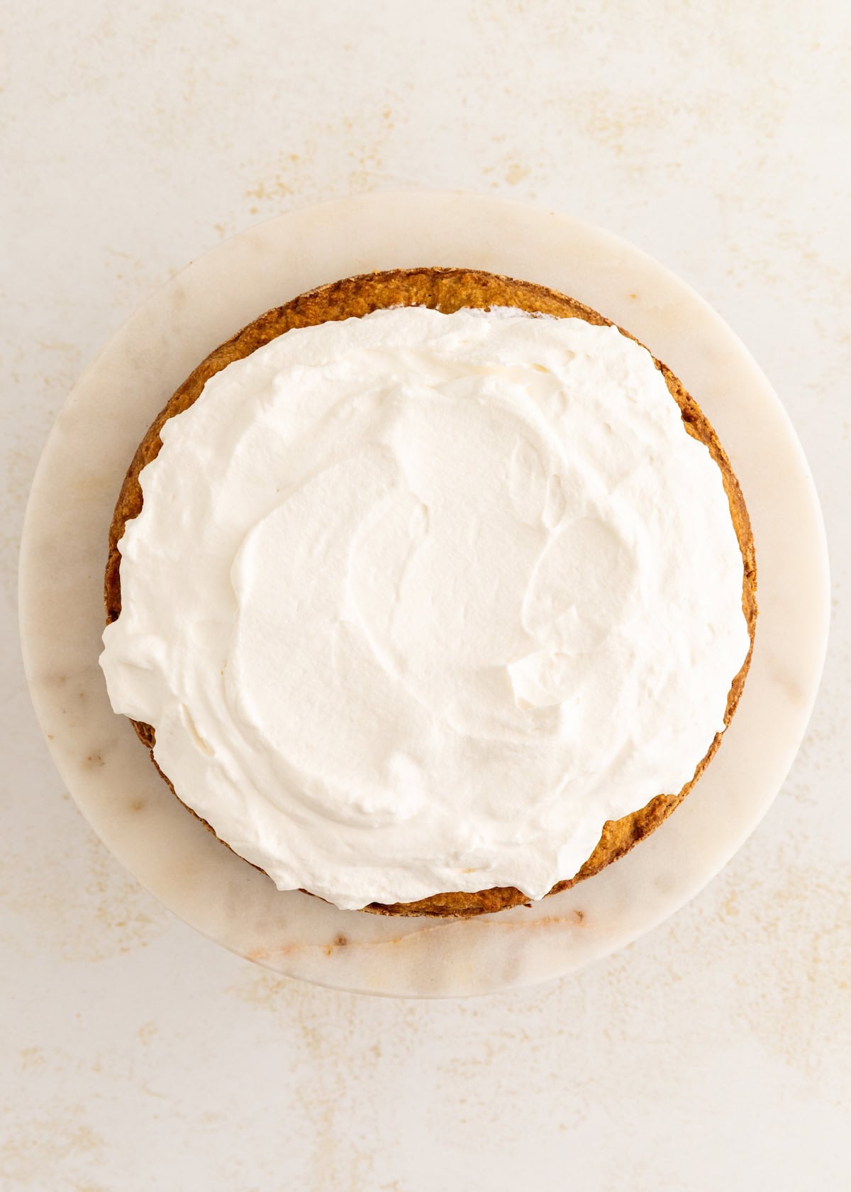 A round cake topped with a layer of whipped cream on a white surface.