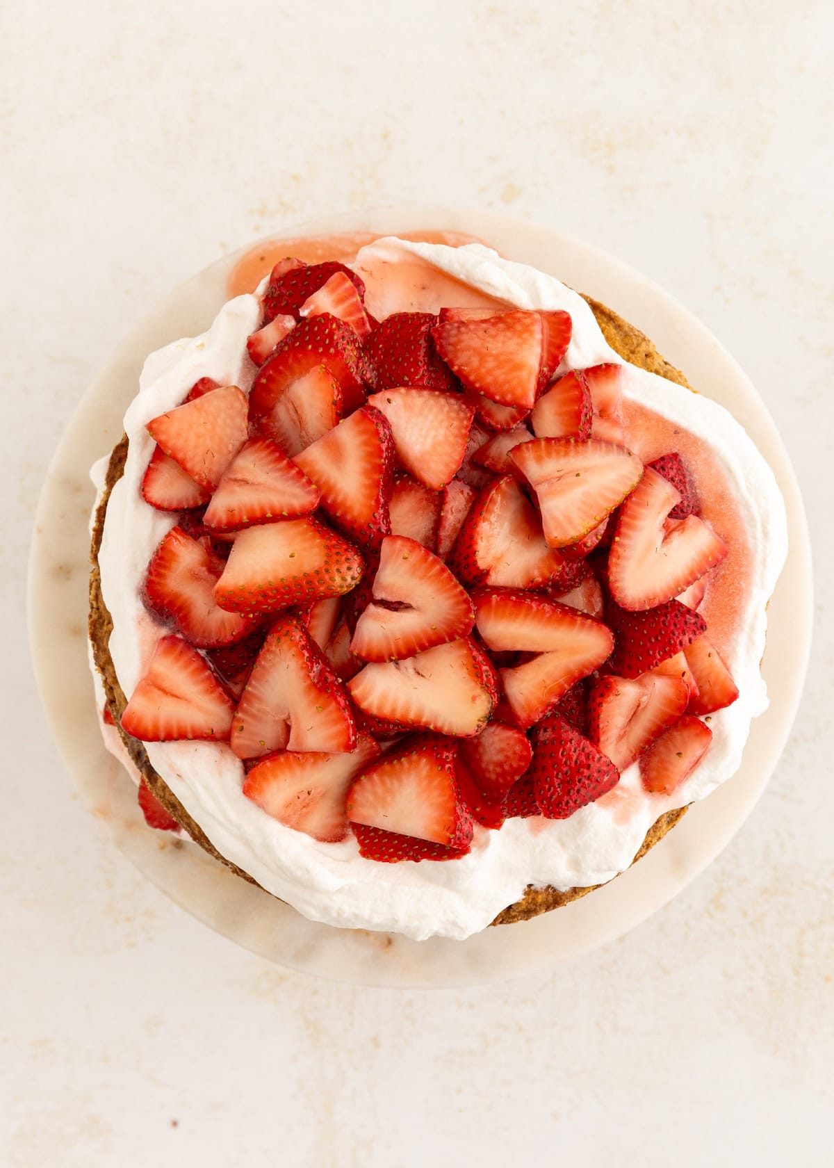 A cake topped with whipped cream and fresh sliced strawberries on a white plate.