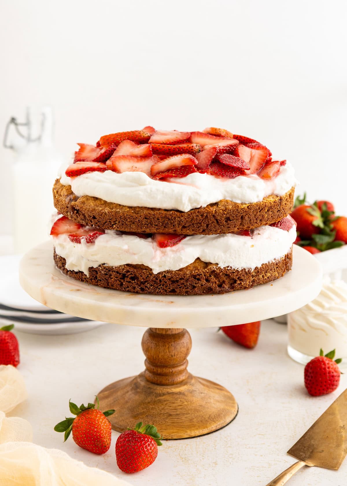 Two-layer strawberry shortcake with whipped cream on a wooden cake stand.