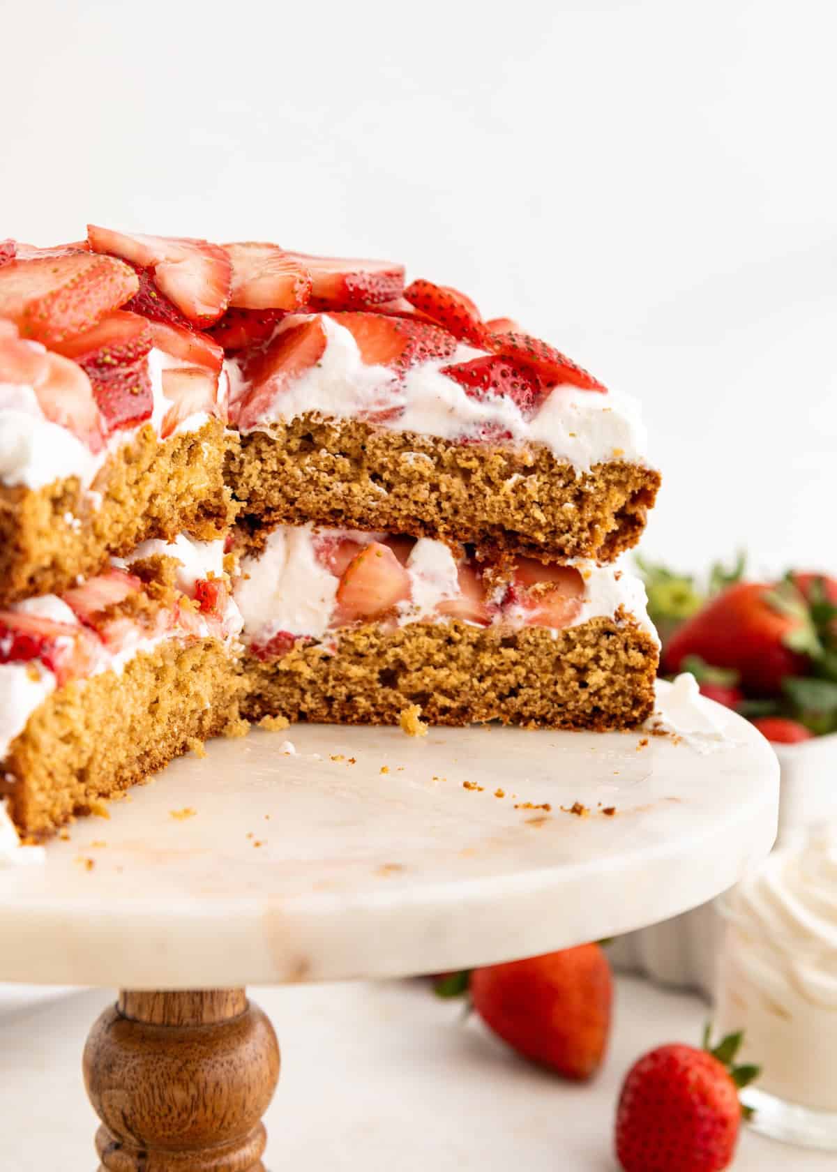 Strawberry shortcake with whipped cream, sliced open on a cake stand, fresh strawberries nearby.
