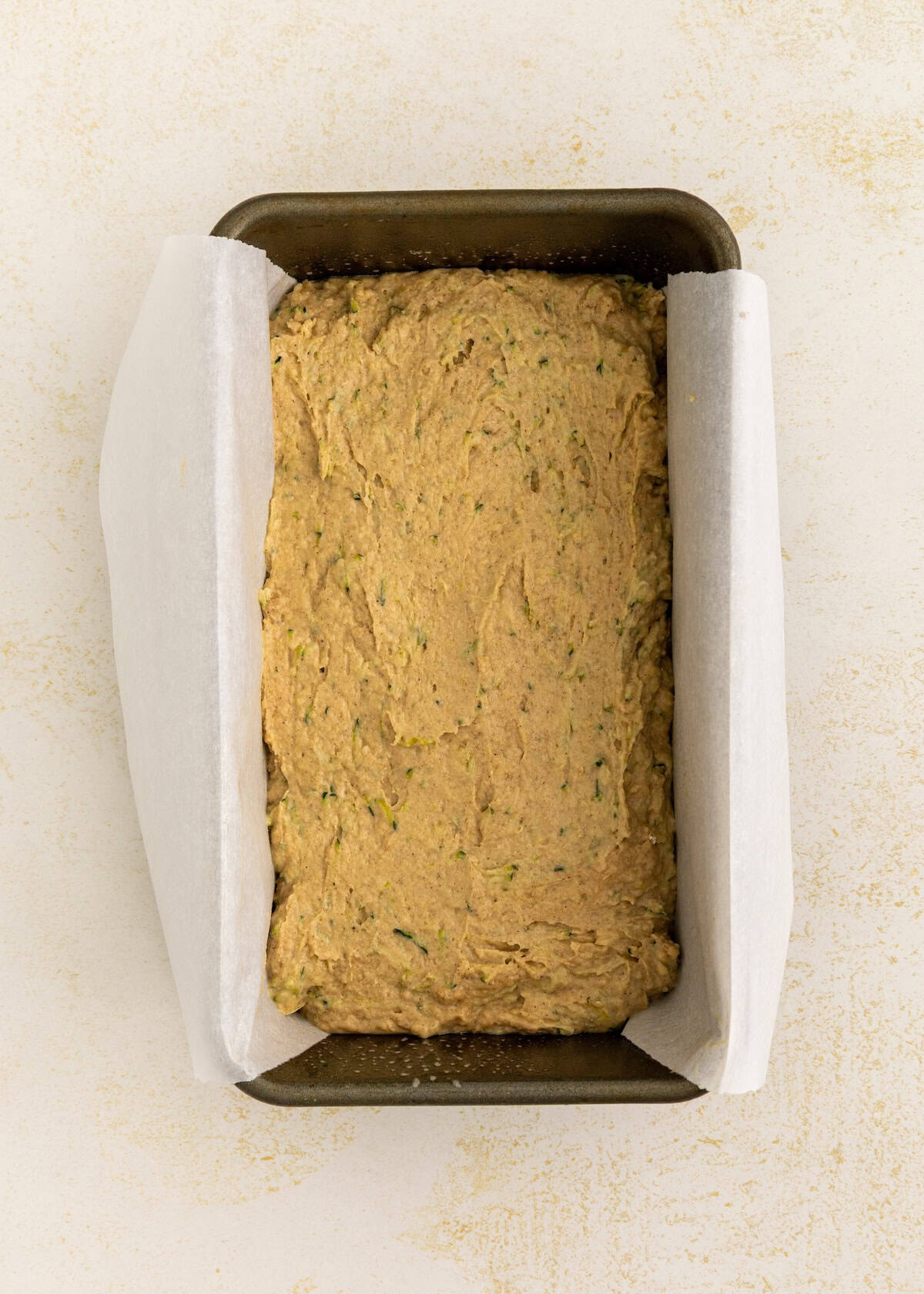 A loaf pan lined with parchment paper filled with unbaked bread batter.
