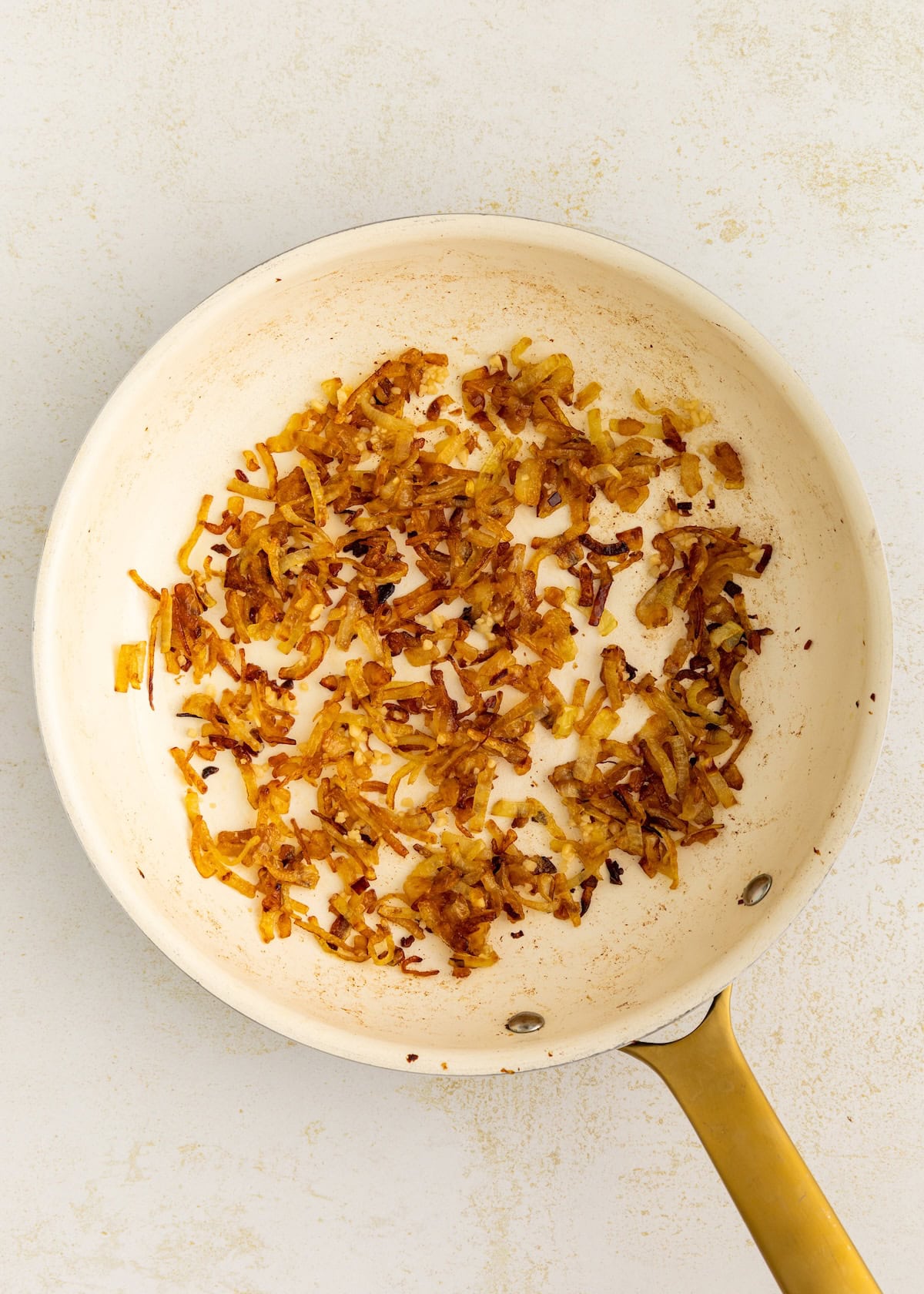 Golden-brown caramelized onions in a white frying pan with a gold handle.