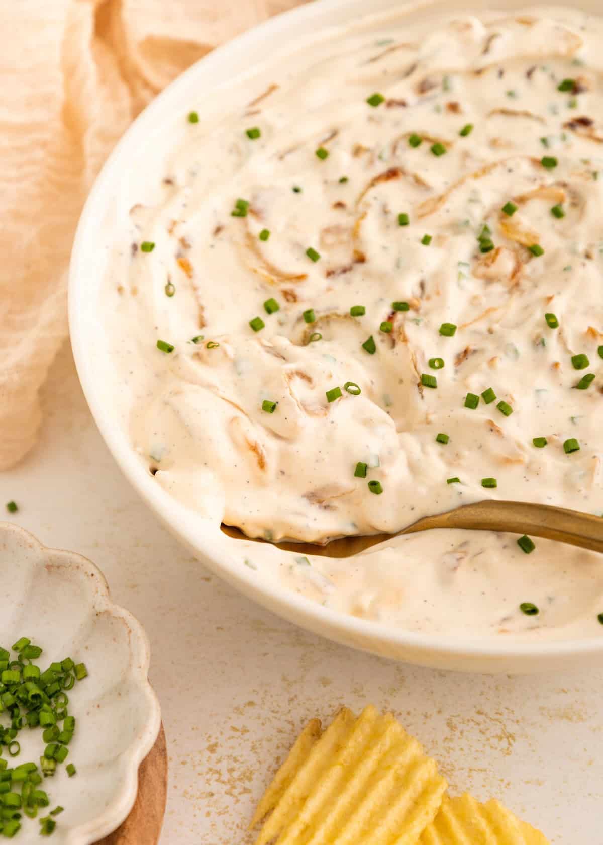 Creamy dip with chopped chives in a bowl, served with ridged potato chips.
