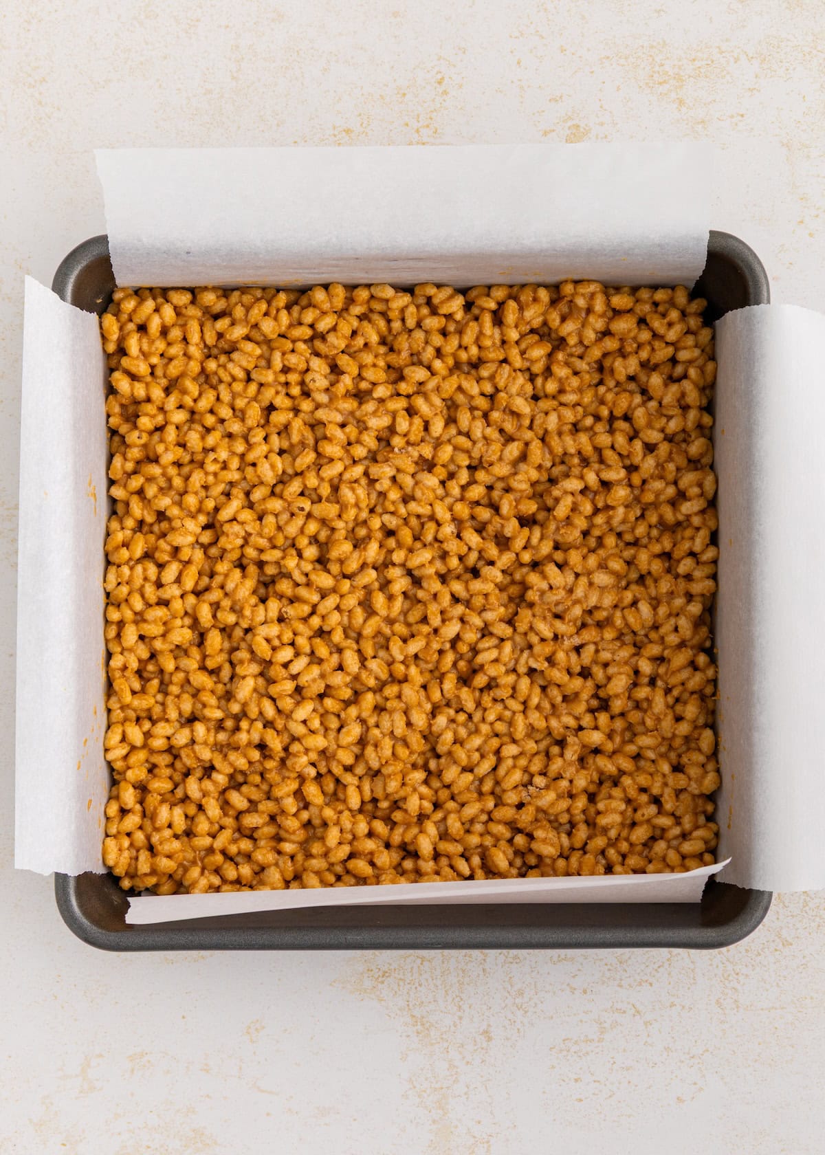 A square pan lined with parchment paper, filled with crispy rice treat mixture.