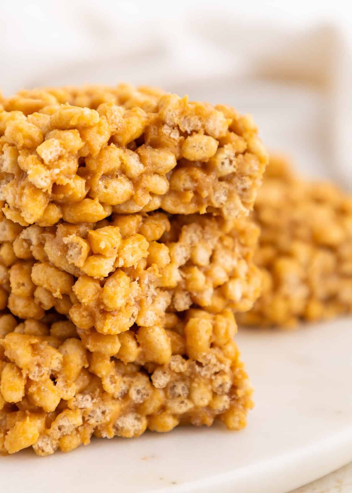 Three stacked peanut butter Rice Krispie treats on a white surface.