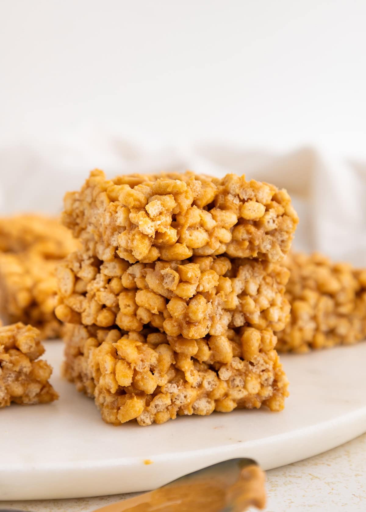 Three stacked rice crispy treats on a white plate with more treats in the background.