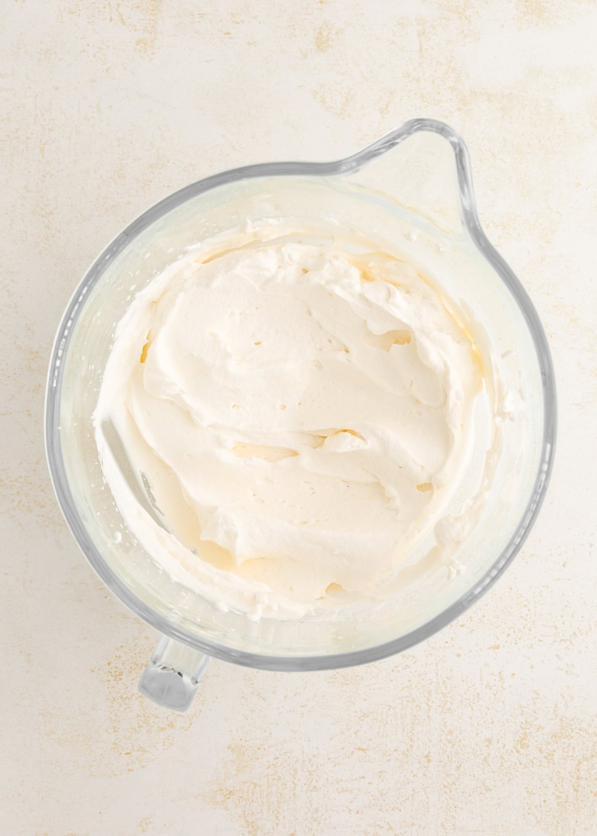 Glass bowl filled with whipped cream on a light, textured surface.