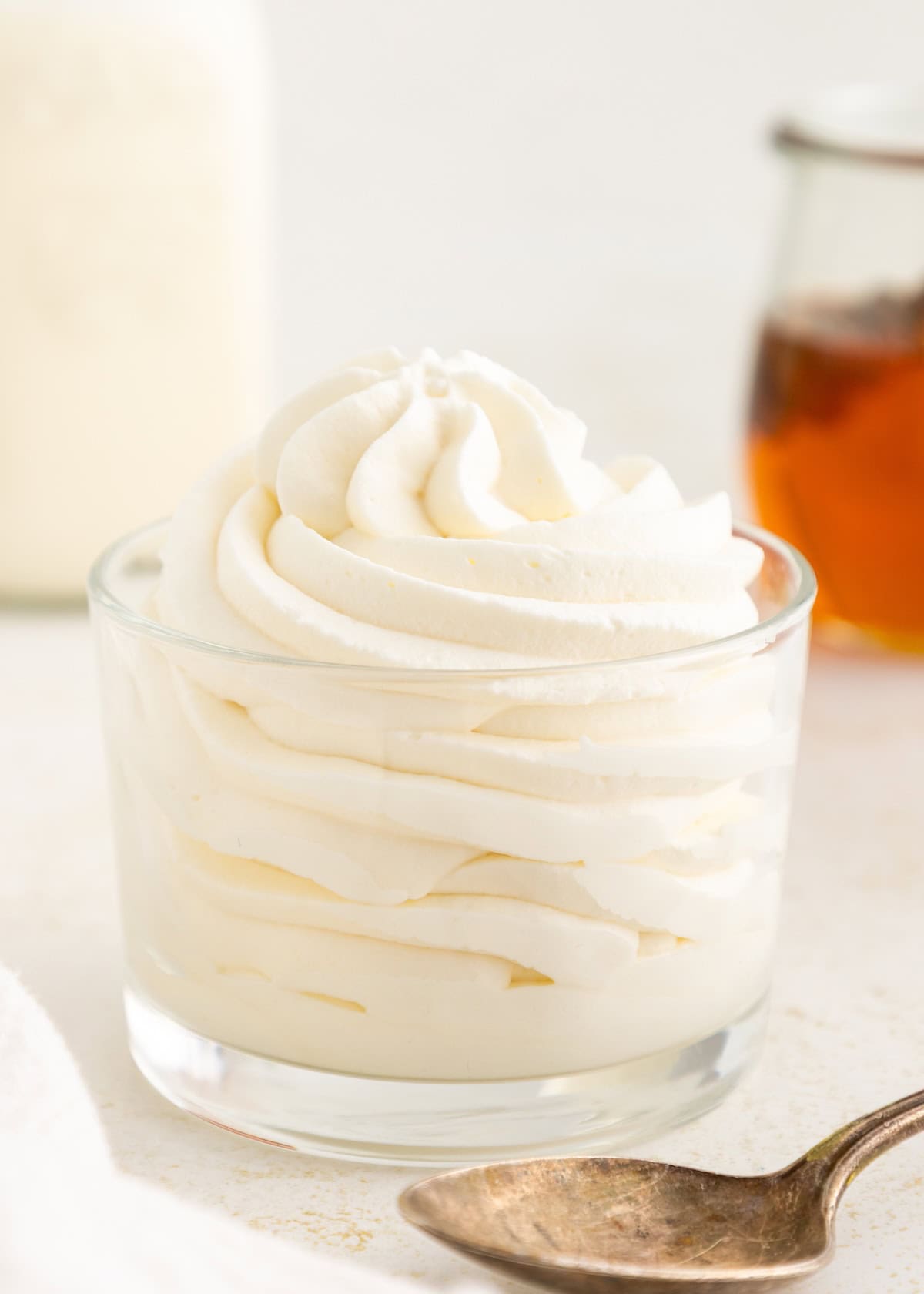 Swirled whipped cream in a glass cup with a spoon in front.