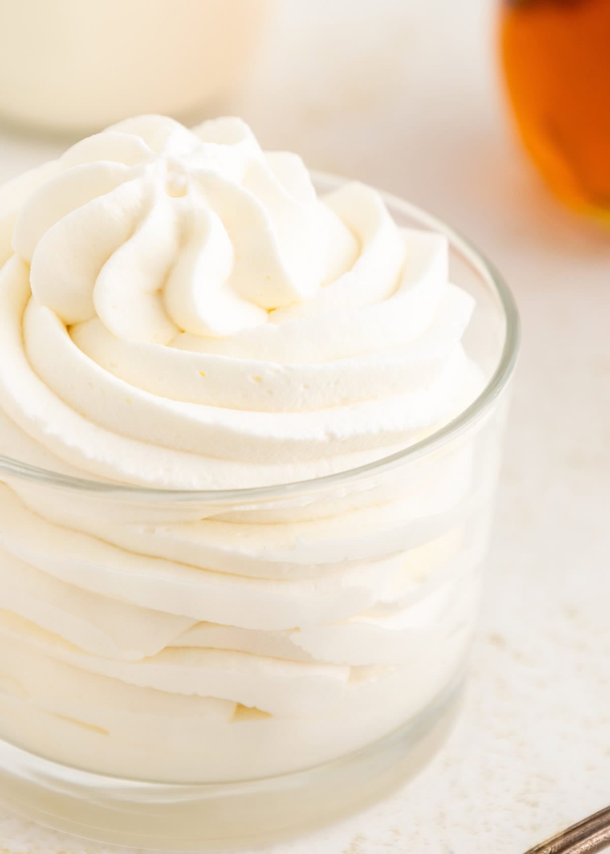 A glass bowl filled with swirled, fluffy whipped cream on a light surface.