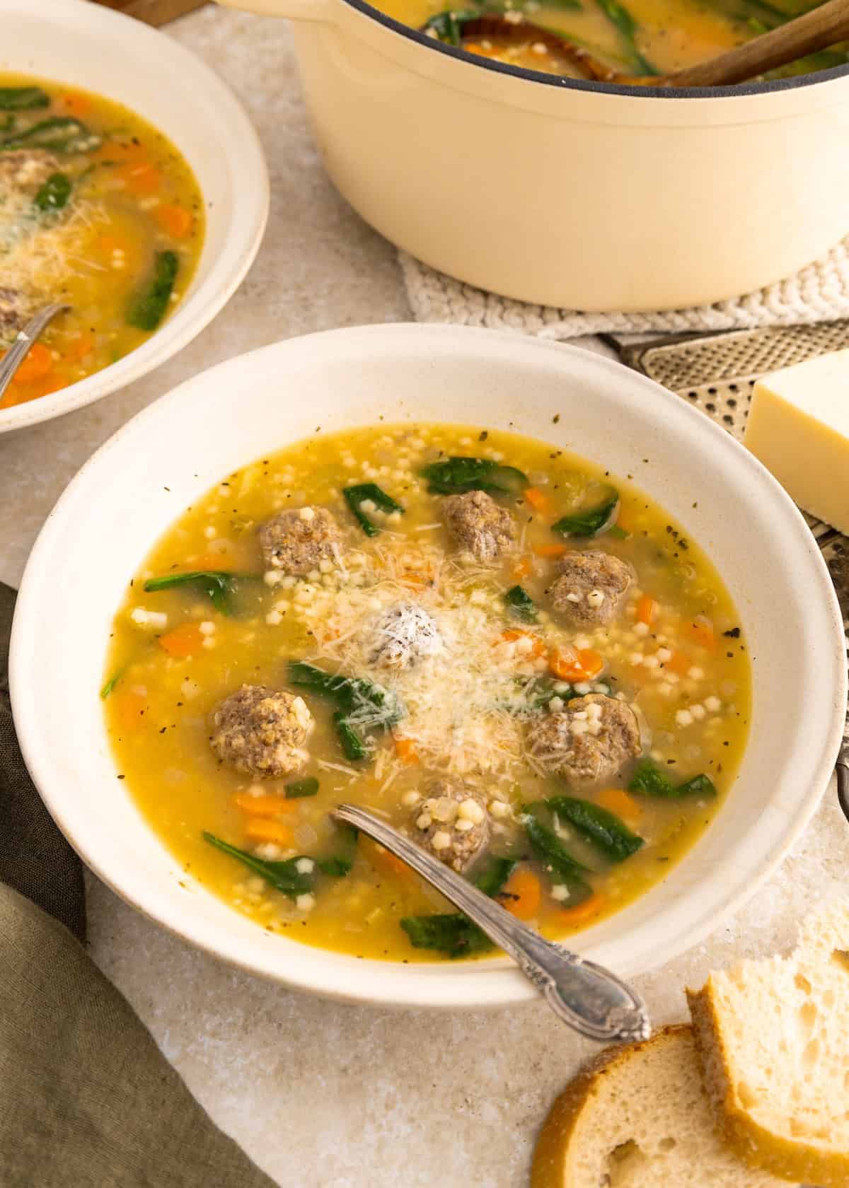 A bowl of Italian Wedding Soup with meatballs, pasta, spinach, and grated cheese on top.
