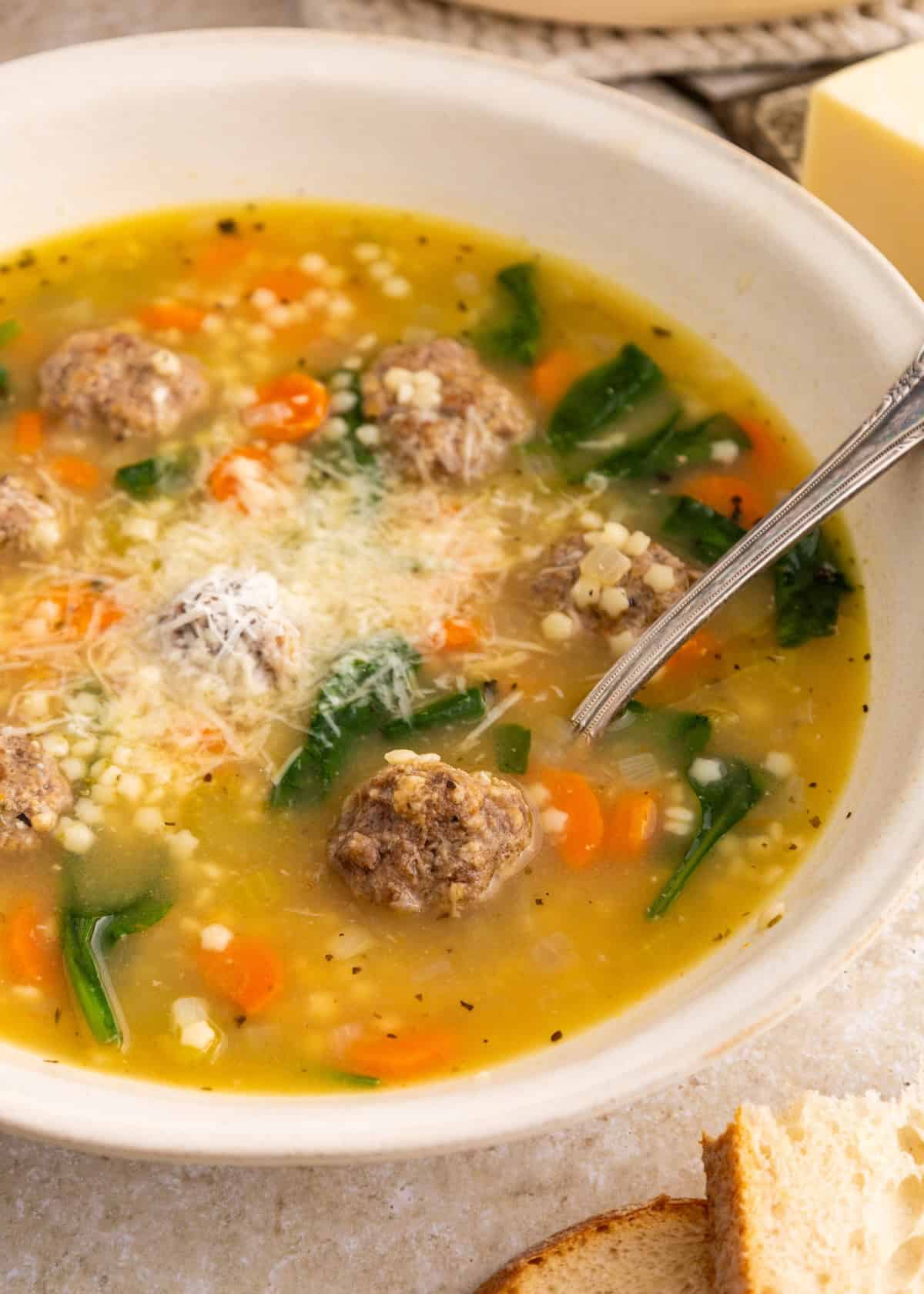 Bowl of Italian Wedding Soup with meatballs, carrots, spinach, and grated cheese on top.