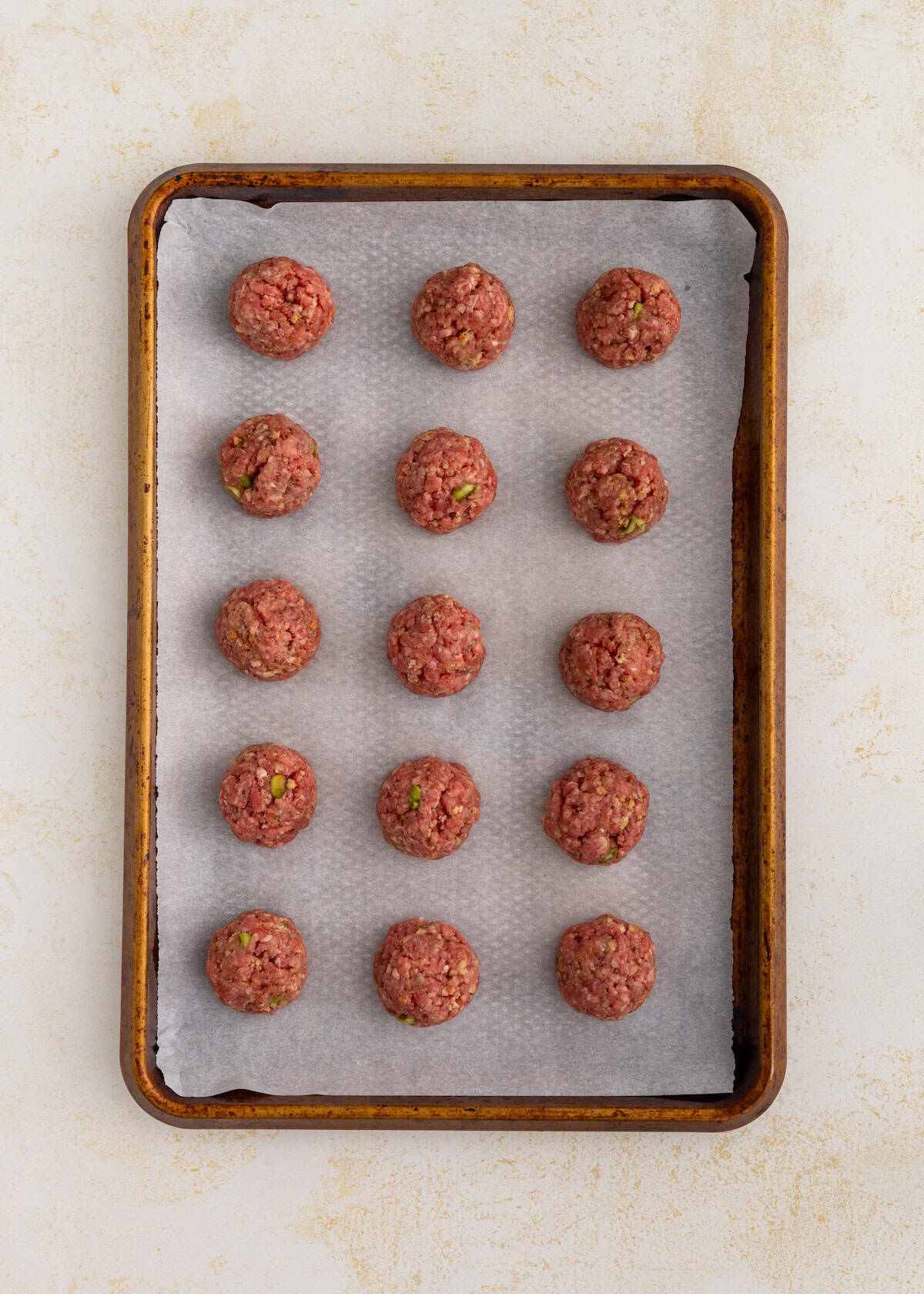 Raw meatballs evenly spaced on a baking sheet lined with parchment paper.