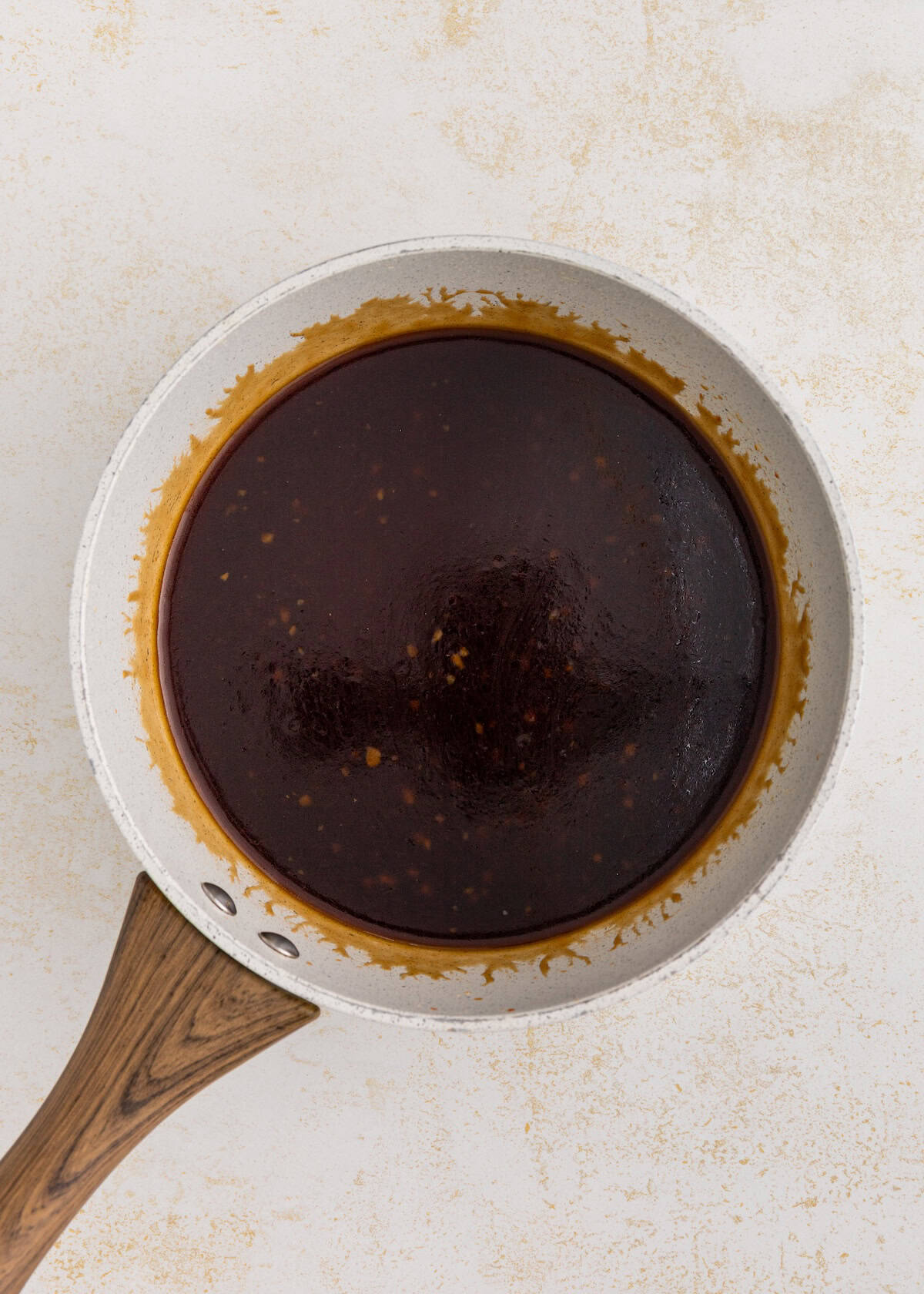 White skillet with thick, dark brown sauce on a light textured background.
