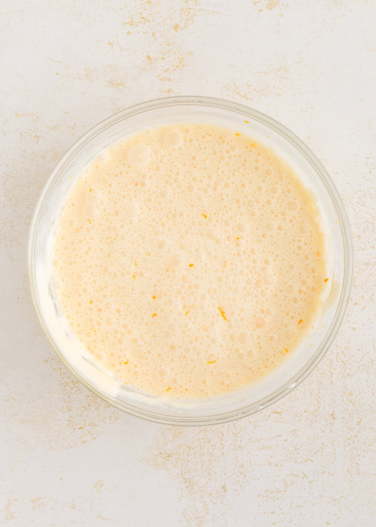 A glass bowl filled with a creamy, frothy liquid on a light surface.