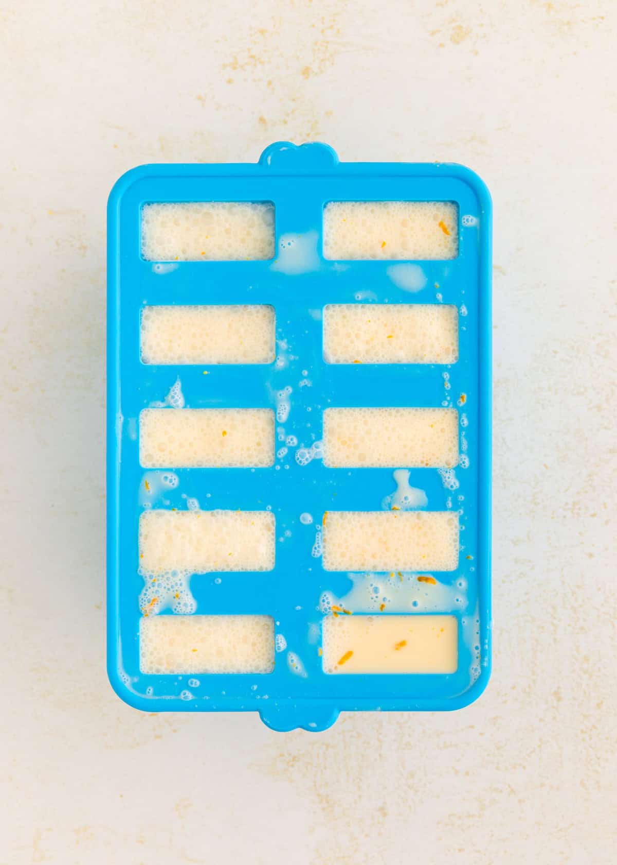 Blue ice cube tray filled with a creamy, frothy liquid with orange specks.