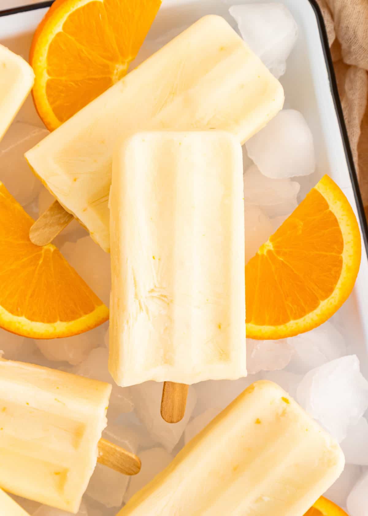 Creamy orange popsicles on ice with fresh orange slices.