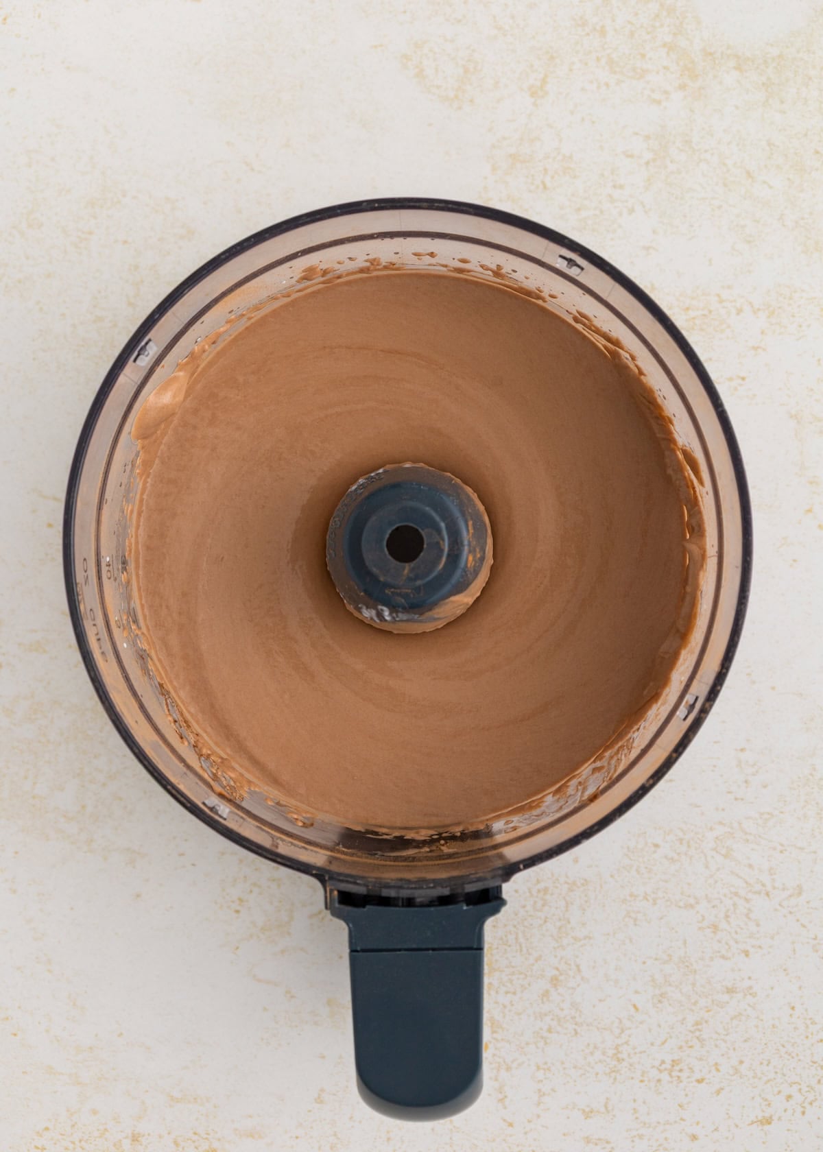Overhead view of chocolate mixture blended in a food processor on a light surface.